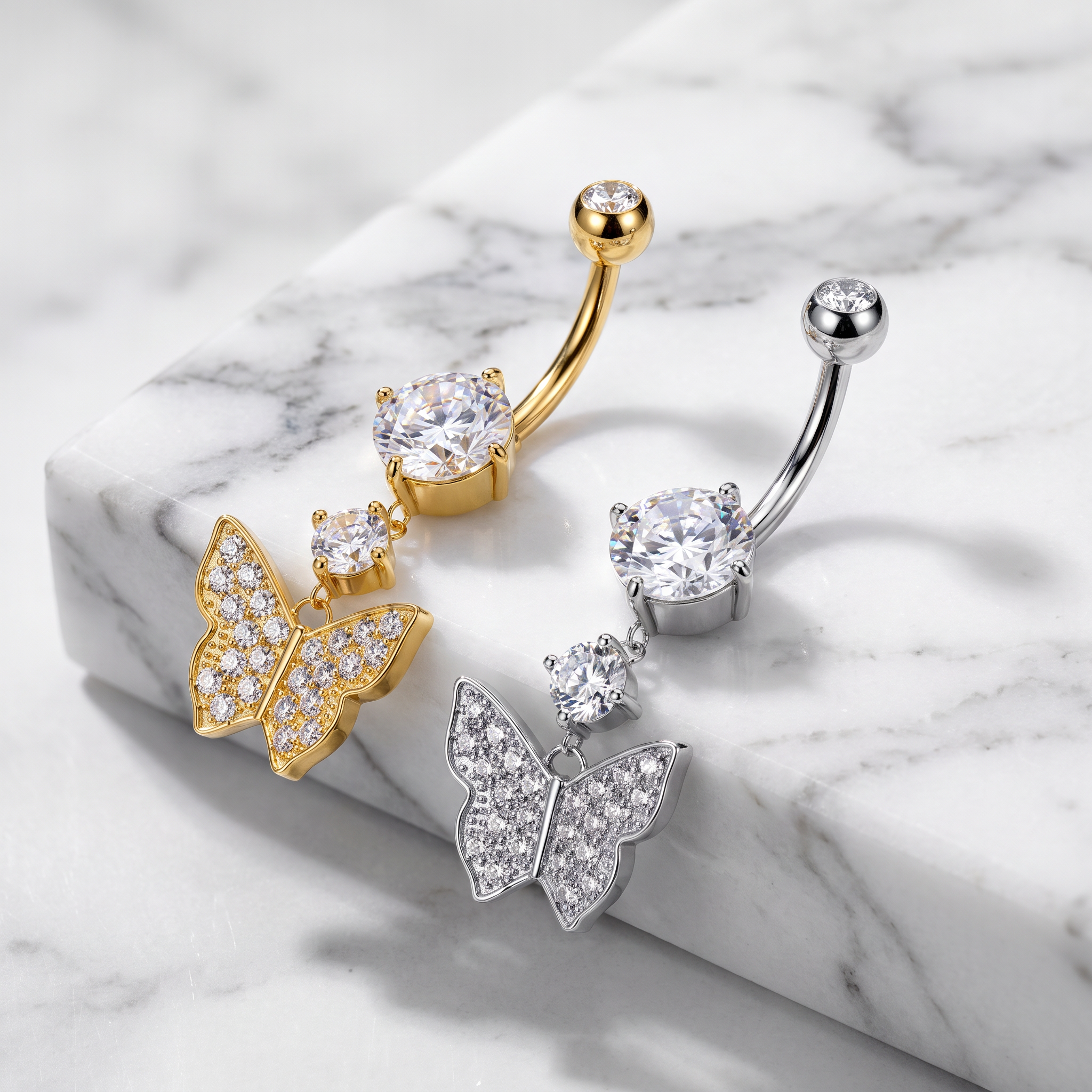 Three butterfly-shaped belly button rings with butterfly backings, shown on a white marble slab. One ring is gold, one is silver, and one is mixed gold and silver.