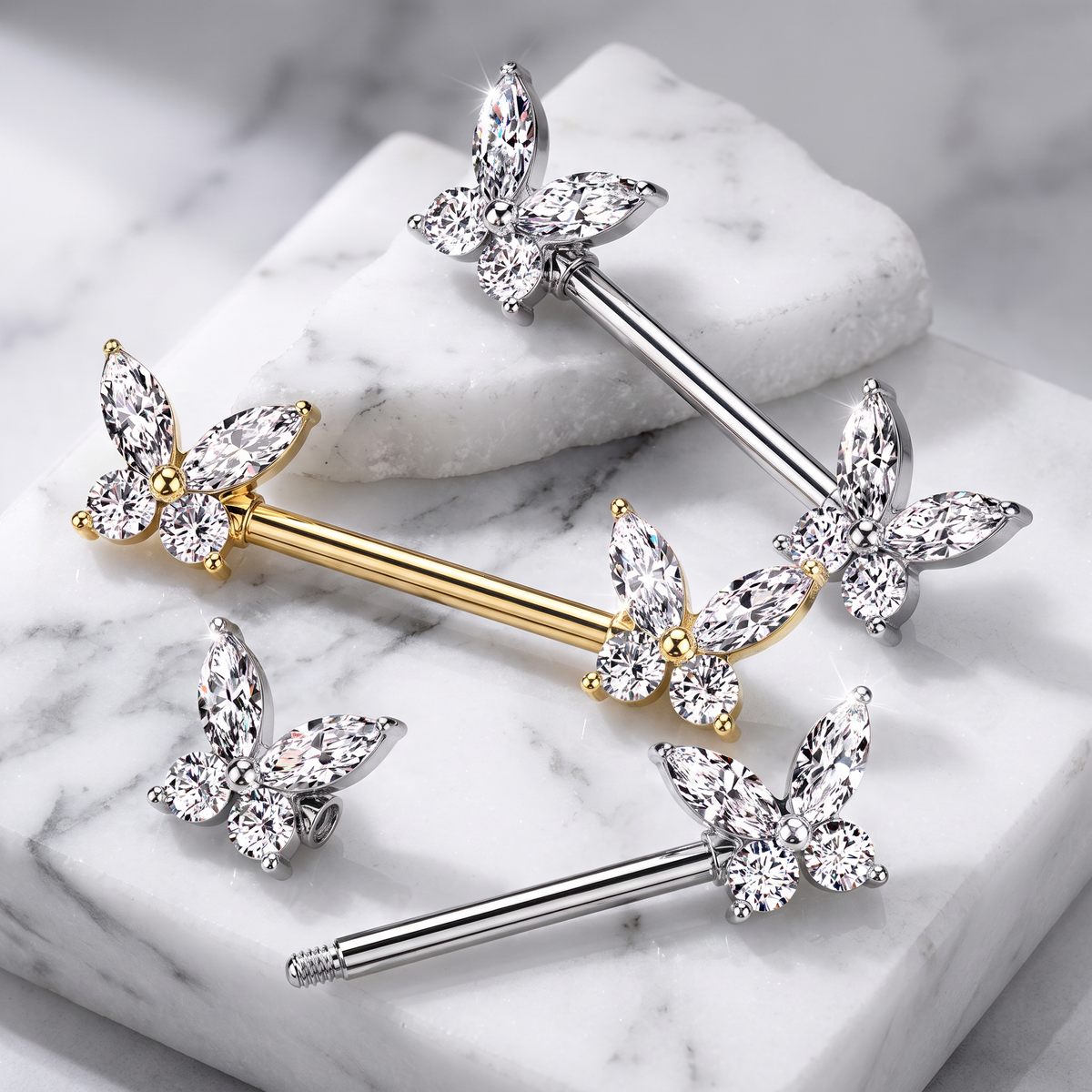 Sterling silver and yellow gold butterfly body jewelry with clear marquise-cut crystals, arranged on a white marble background.