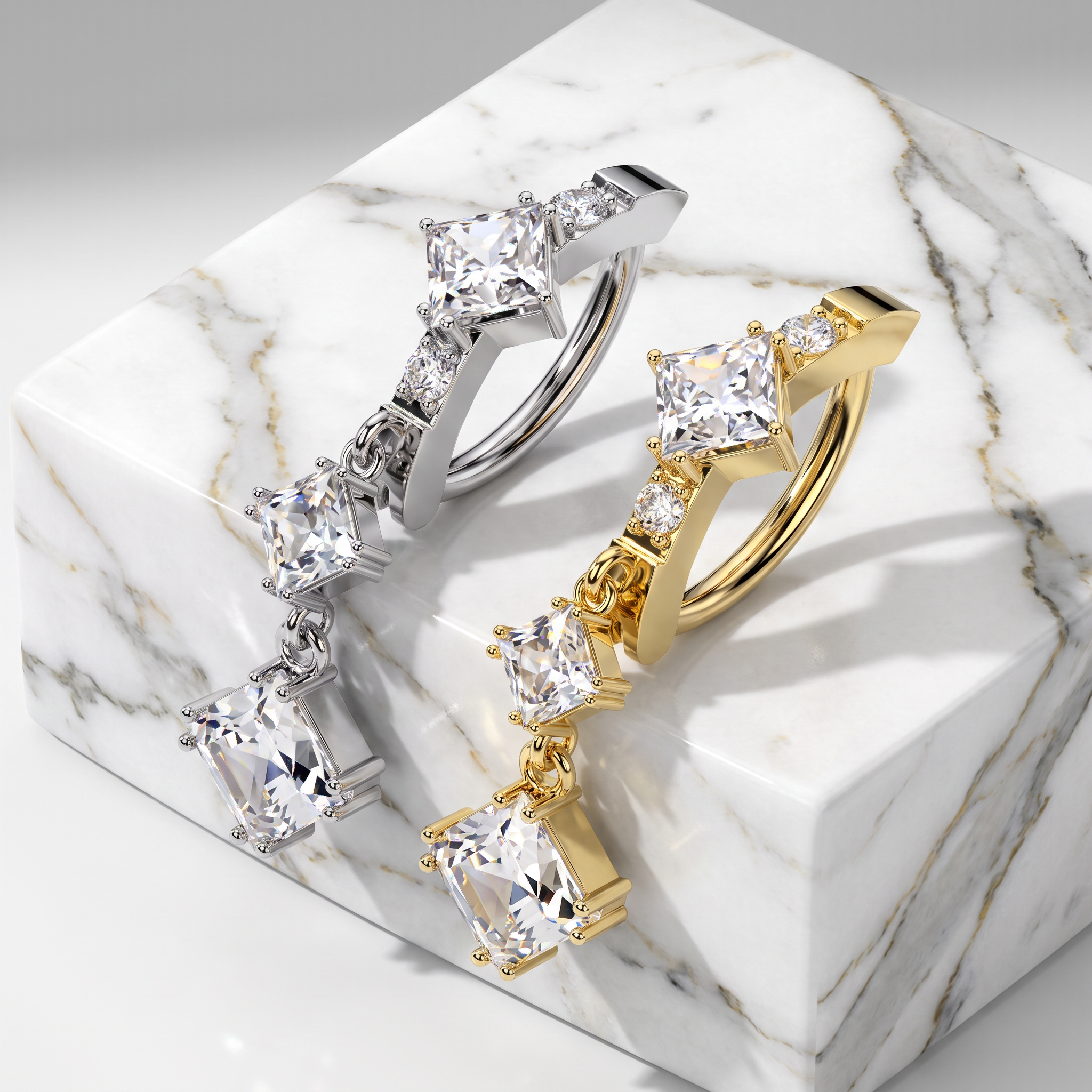 Two statement earrings displayed on a white marble block, one in silver-tone metal and one in yellow gold-tone metal, each featuring a large princess-cut clear gemstone and smaller accent stones.