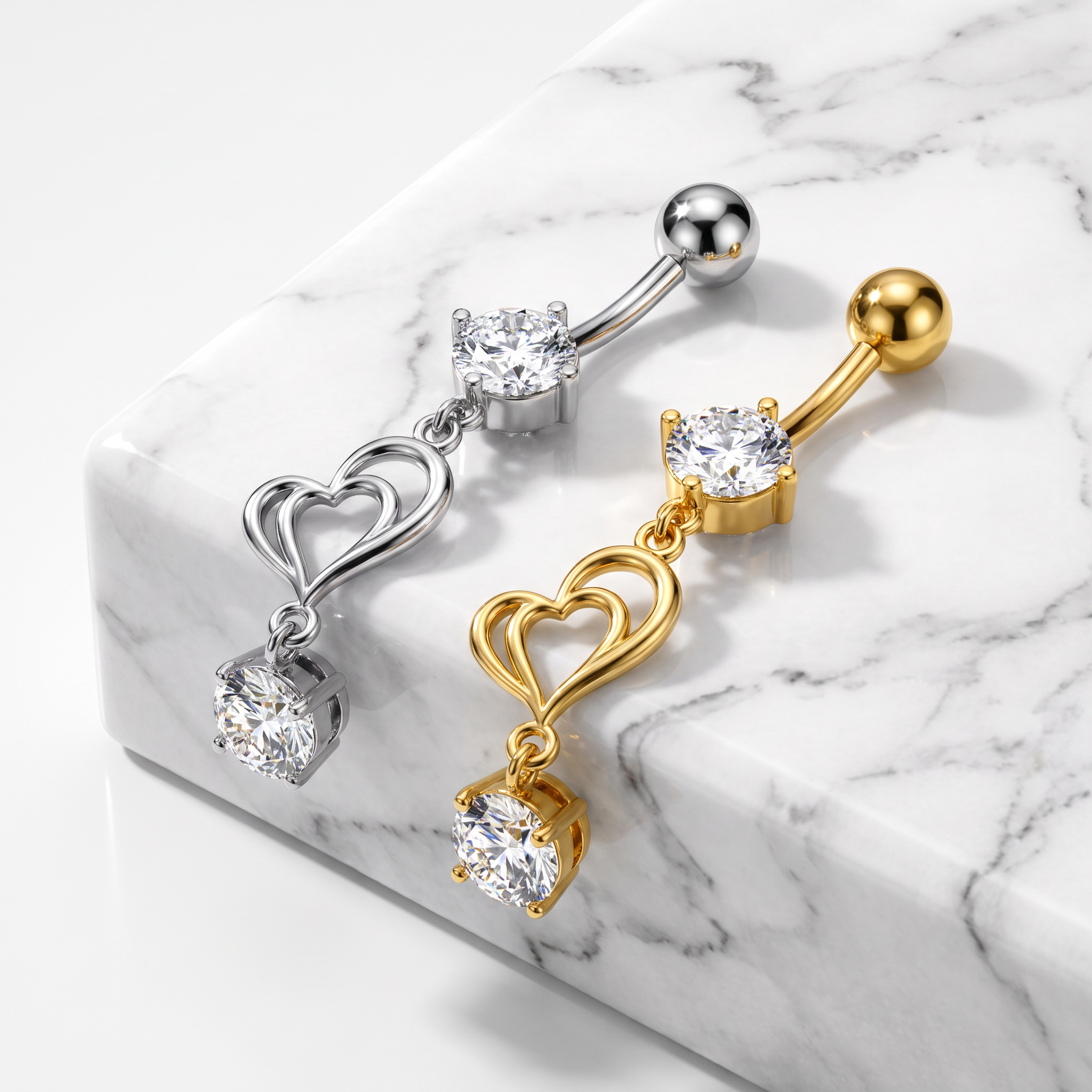 Two curved barbell body jewelry piercings with double heart charms and clear gemstones, shown on a white marble block. One is silver-toned and one is gold-toned.
