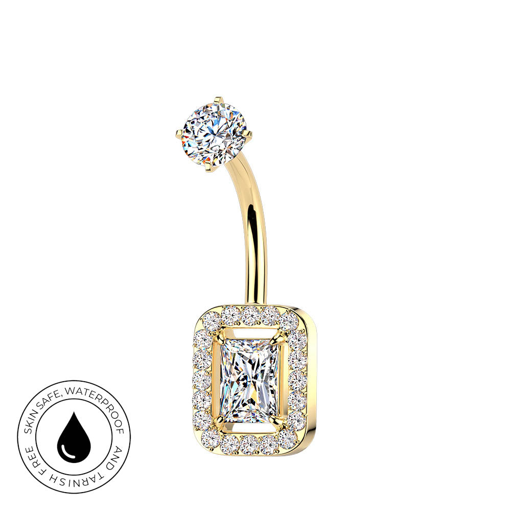 Gold curved barbell navel piercing ring with a rectangular halo of small clear stones and a central princess-cut clear stone, shown on a white background with a small circular skin-safe waterproof badge in the lower left.