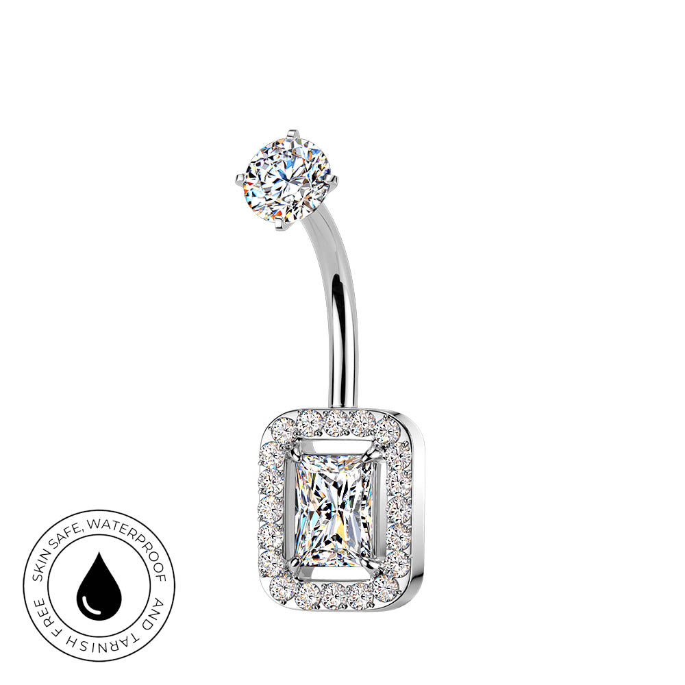 A silver-toned curved barbell belly button ring with a rectangular halo setting and a central princess-cut clear gemstone, shown on a white background with a small circular skin-safe waterproof badge in the lower left.