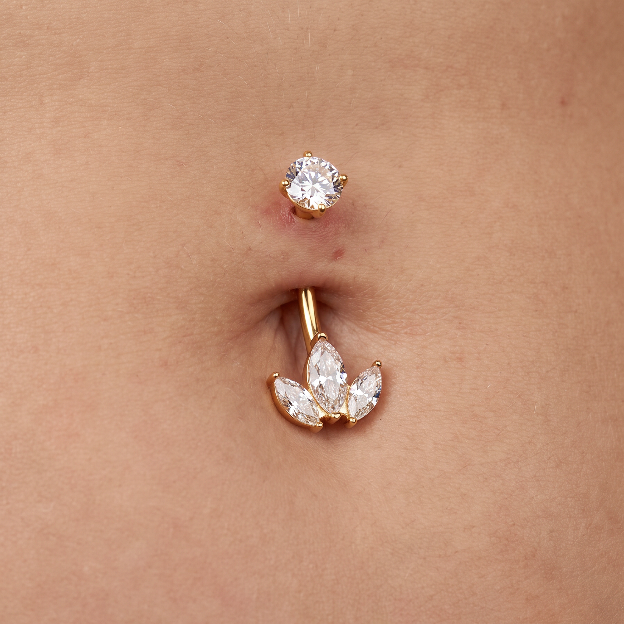 Gold belly button ring with a single round clear rhinestone above a barbell stud featuring three marquise-cut clear rhinestones in a leaf cluster, shown on a person's skin.