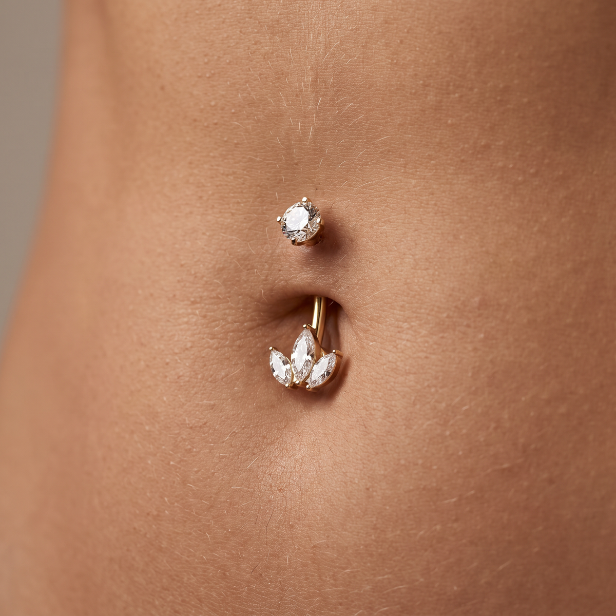 Close-up of a gold navel piercing with clear rhinestone accents, shown worn on a person's abdomen.