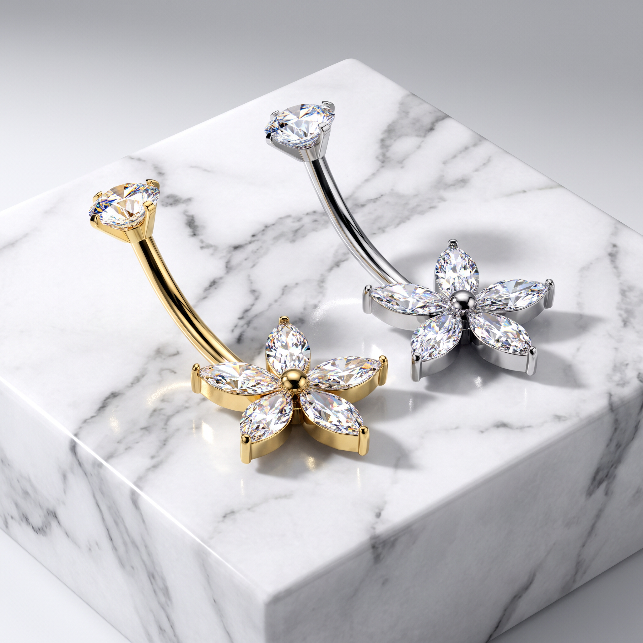 Two flower-shaped belly button rings with clear marquise-cut gemstones, one in yellow gold and one in silver, displayed on a white marble block against a light gray background.