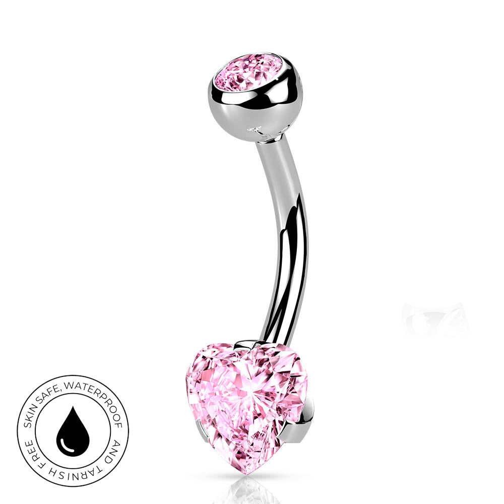 A curved barbell belly button ring with a polished silver-tone metal and a large, faceted pink heart-shaped crystal on one end and a smaller round pink crystal on the other. A circular badge on the bottom left highlights 'Skin Safe, Waterproof' features.