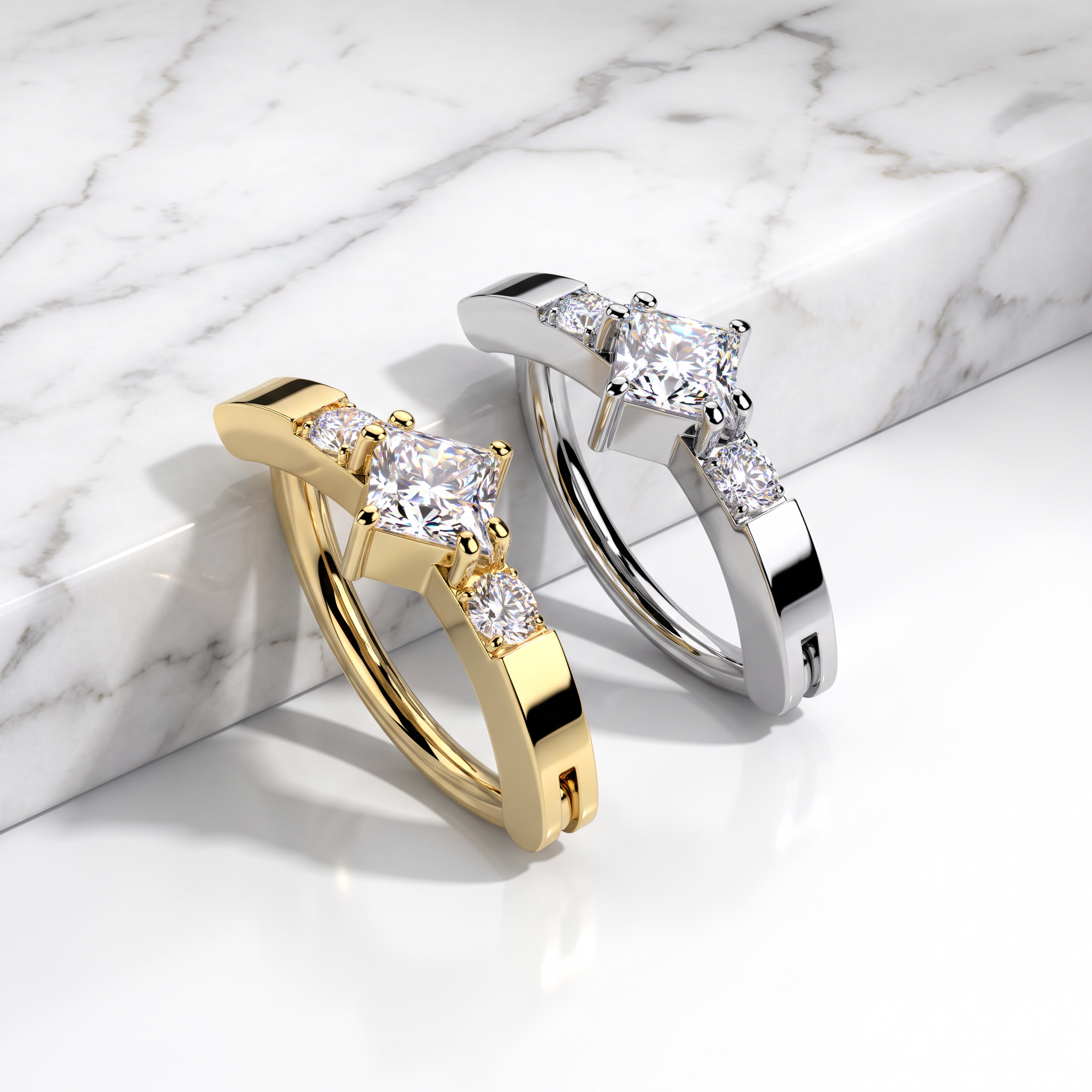 Two huggie-style hoop rings with marquise-cut center stones and small side stones, shown in yellow gold and silver-tone metal on a white marble surface.