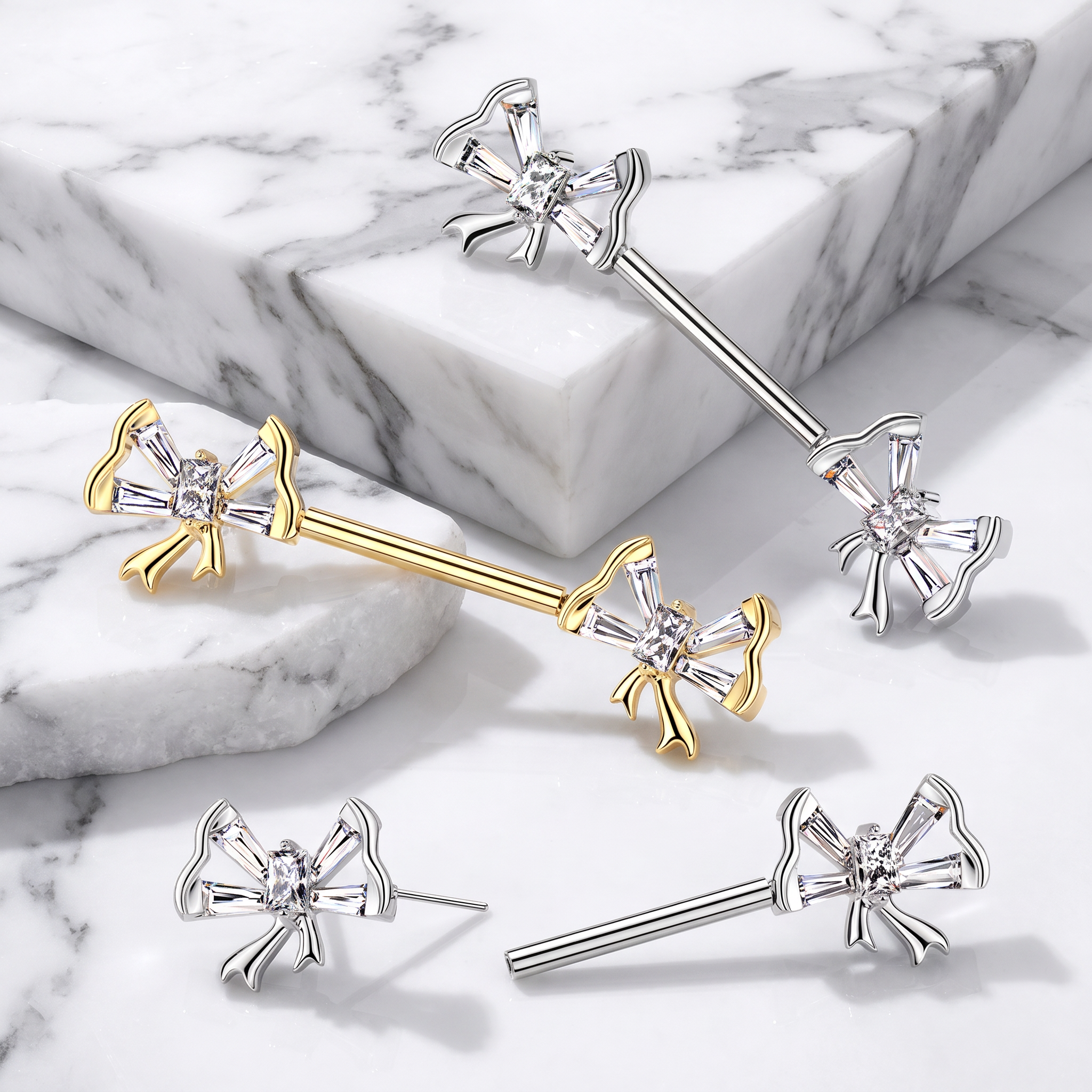 Sterling silver and yellow gold barbell earrings with a crystal-accented bow design, displayed on a white and gray marble background.