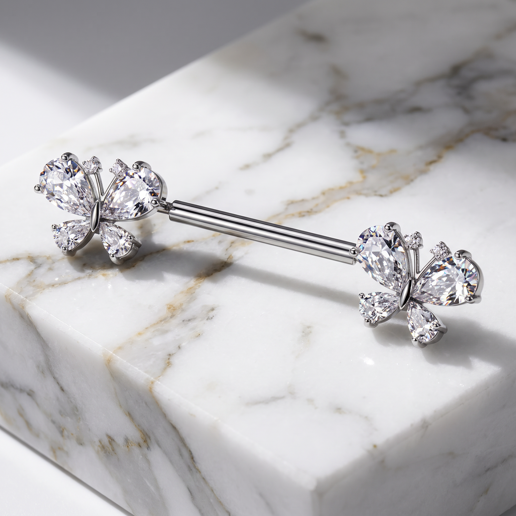 A silver-toned barbell piercing jewelry piece with butterfly-shaped end studs set with clear gemstones, displayed on a white marble block.