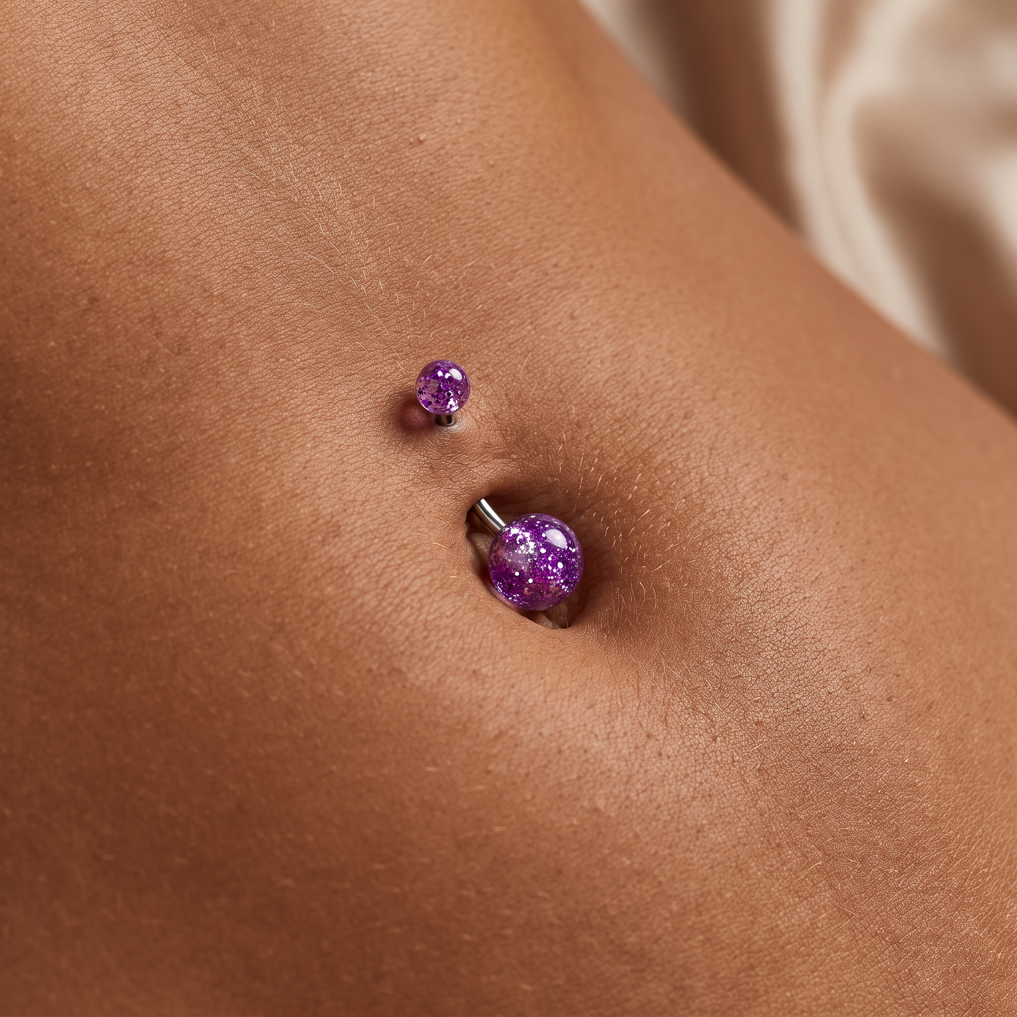 A close-up of a person's navel wearing two purple glitter stud and barbell belly button piercings.