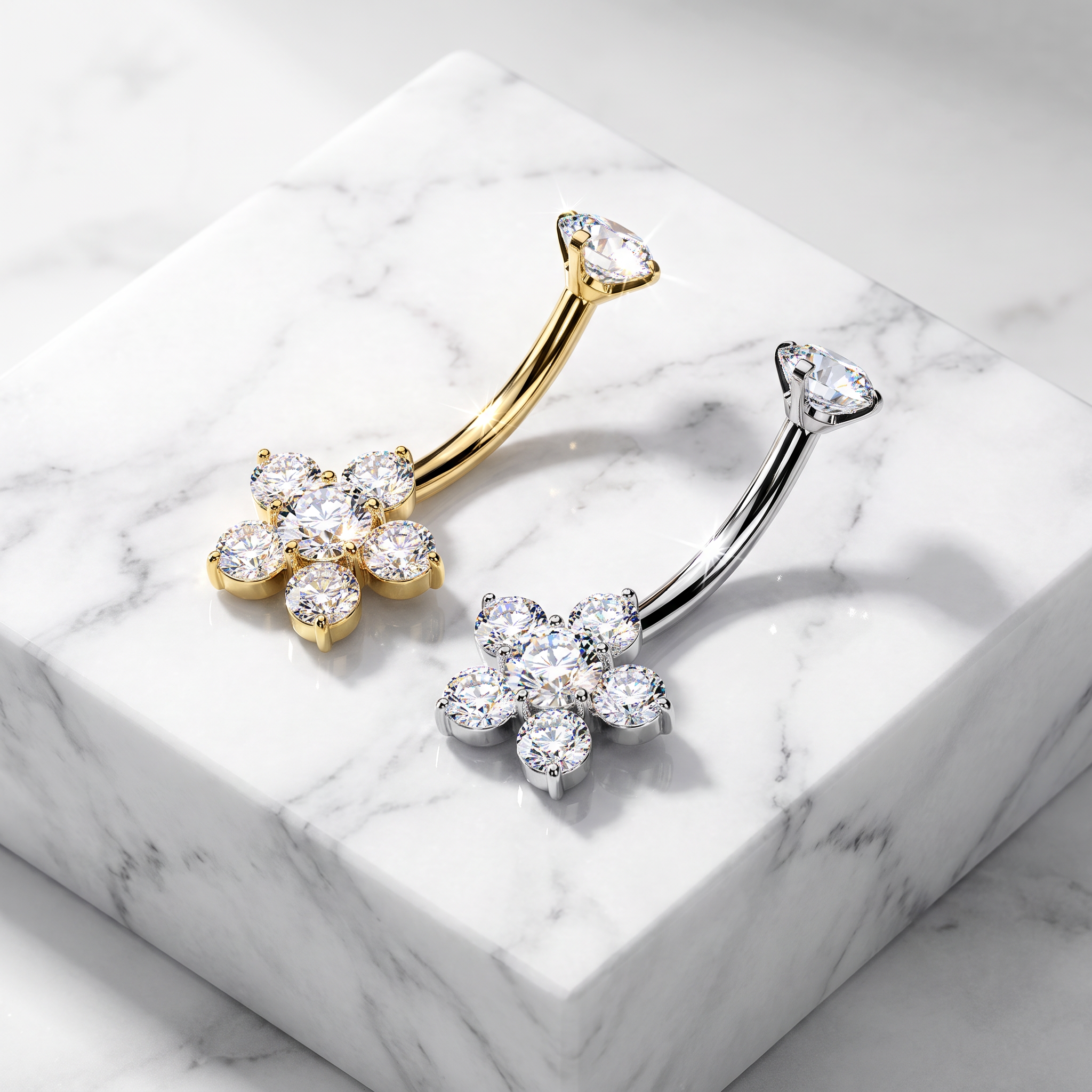 Two flower-shaped belly button rings with clear cubic zirconia stones, one in yellow gold and one in silver, displayed on a white marble block.