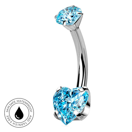 A curved silver-toned belly button ring with a large light blue heart-shaped crystal on one end and a round light blue crystal on the other, shown on a white background with a small circular skin-safe waterproof badge in the lower left.