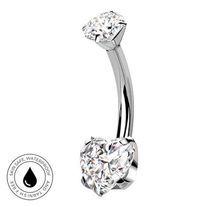 A curved barbell belly button ring with a large heart-shaped clear gemstone on one end and a round clear gemstone on the other, shown on a white background with a small circular skin-safe waterproof badge in the lower left.