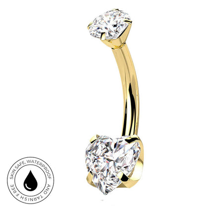 A curved yellow gold navel piercing ring with two clear gemstones, one round and one heart-shaped, shown on a white background with a circular skin-safe waterproof badge in the bottom-left corner.