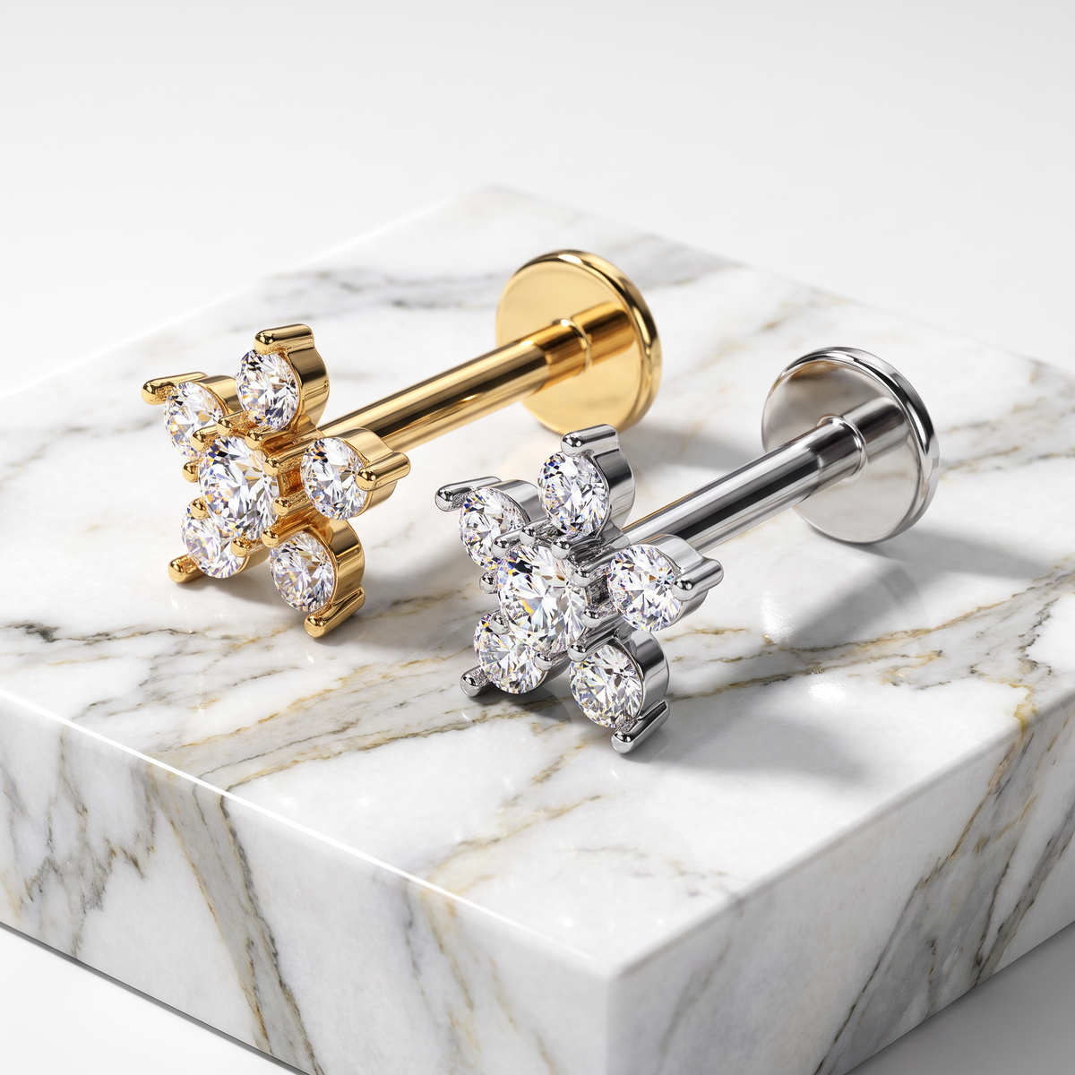 Two flower-shaped stud earrings displayed on a white marble block. One earring has a gold post and cluster, and the other has a silver post and cluster, both set with clear gemstones.