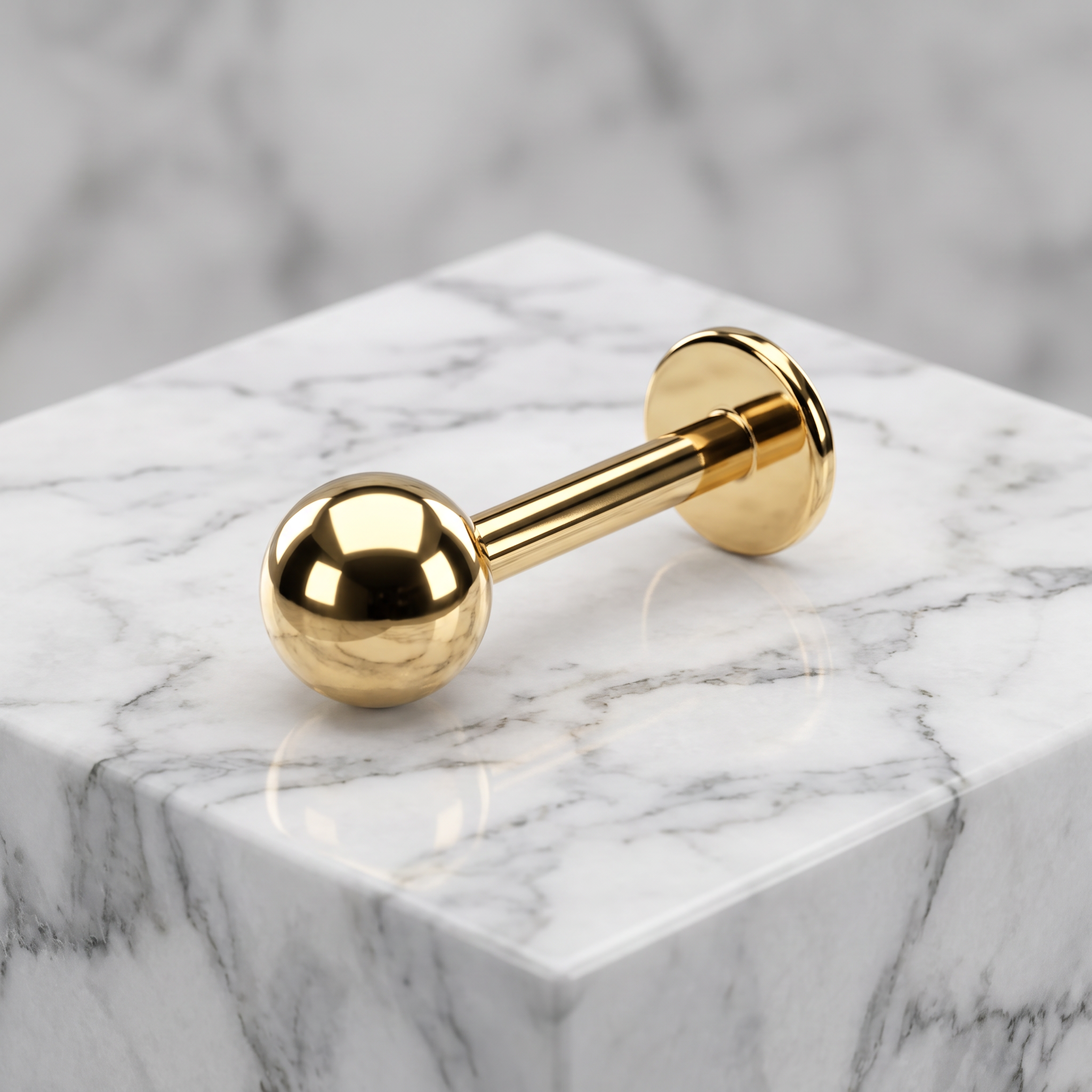 A gold-tone labret piercing stud with a polished ball end and flat back, displayed on a white marble cube against a matching marble background.