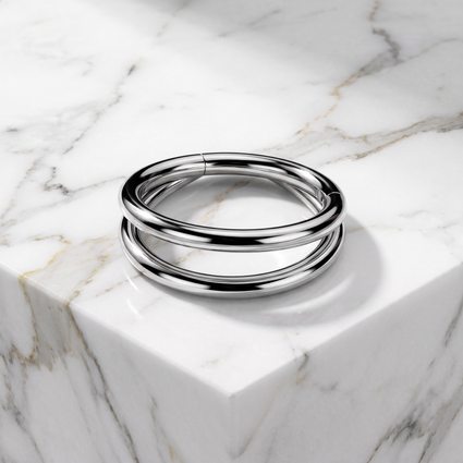 A polished silver-toned metal cuff bracelet with three parallel bands, resting on a white marble block with gray veining.