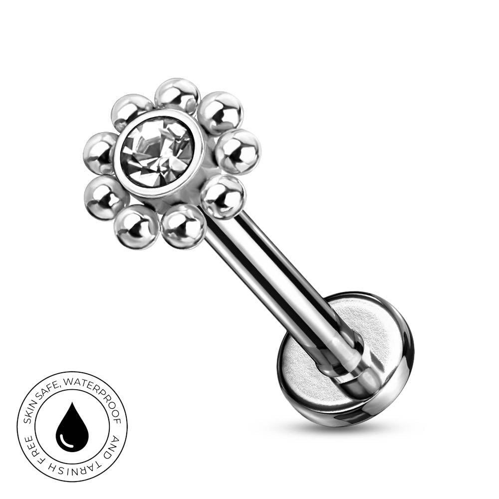 A silver-toned labret piercing barbell with a flower-like top featuring a clear faceted gemstone surrounded by small metallic beads, shown on a white background with a circular 'SkinSafe Waterproof' badge in the lower left.
