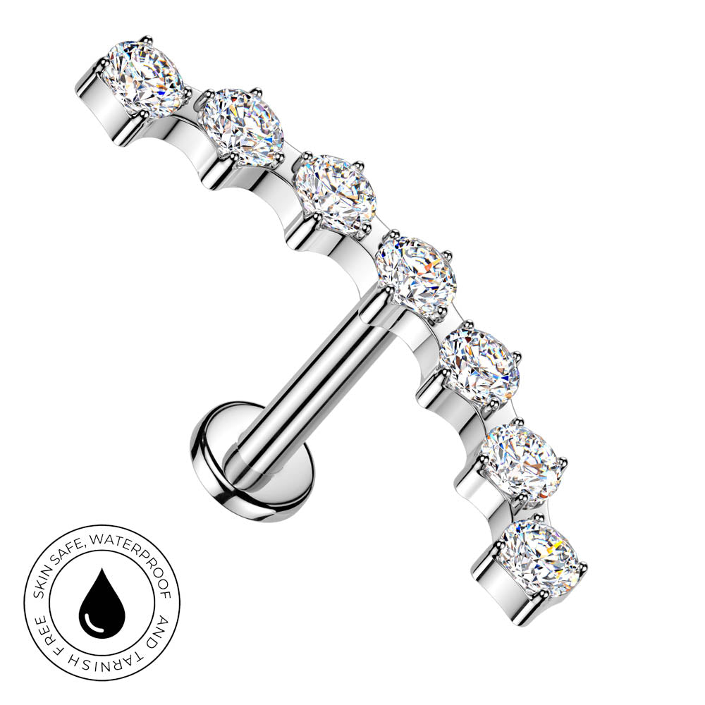 A silver-toned labret piercing barbell featuring seven clear, round-cut cubic zirconia stones in a row. A circular badge in the bottom-left corner highlights its 'Skin Safe, Waterproof' and 'Tarnish Free' qualities.