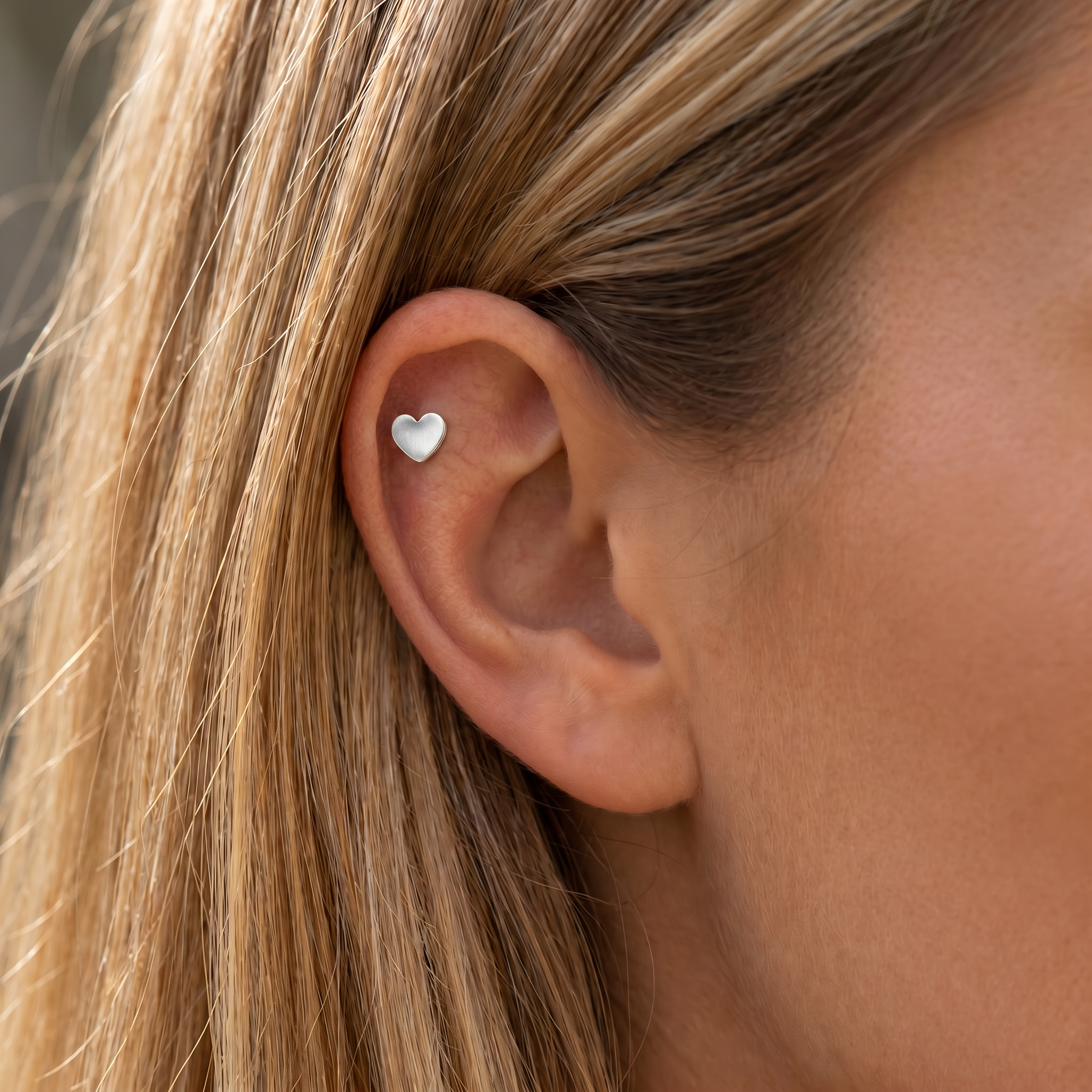 A close-up of a woman's ear wearing a small white heart-shaped stud earring.