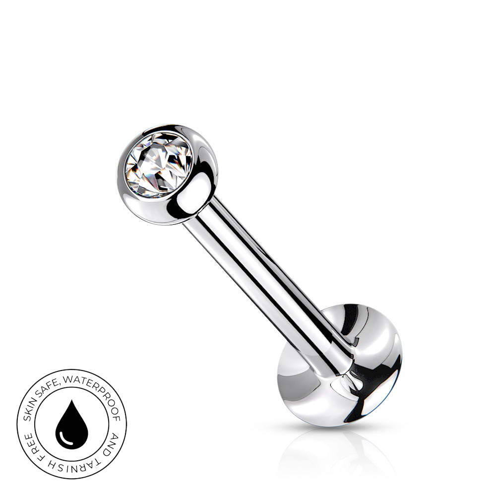 A silver-toned curved barbell piercing stud with a clear faceted gemstone on one end and a round polished back, shown on a white background with a small circular 'skin-safe waterproof' badge in the lower left.