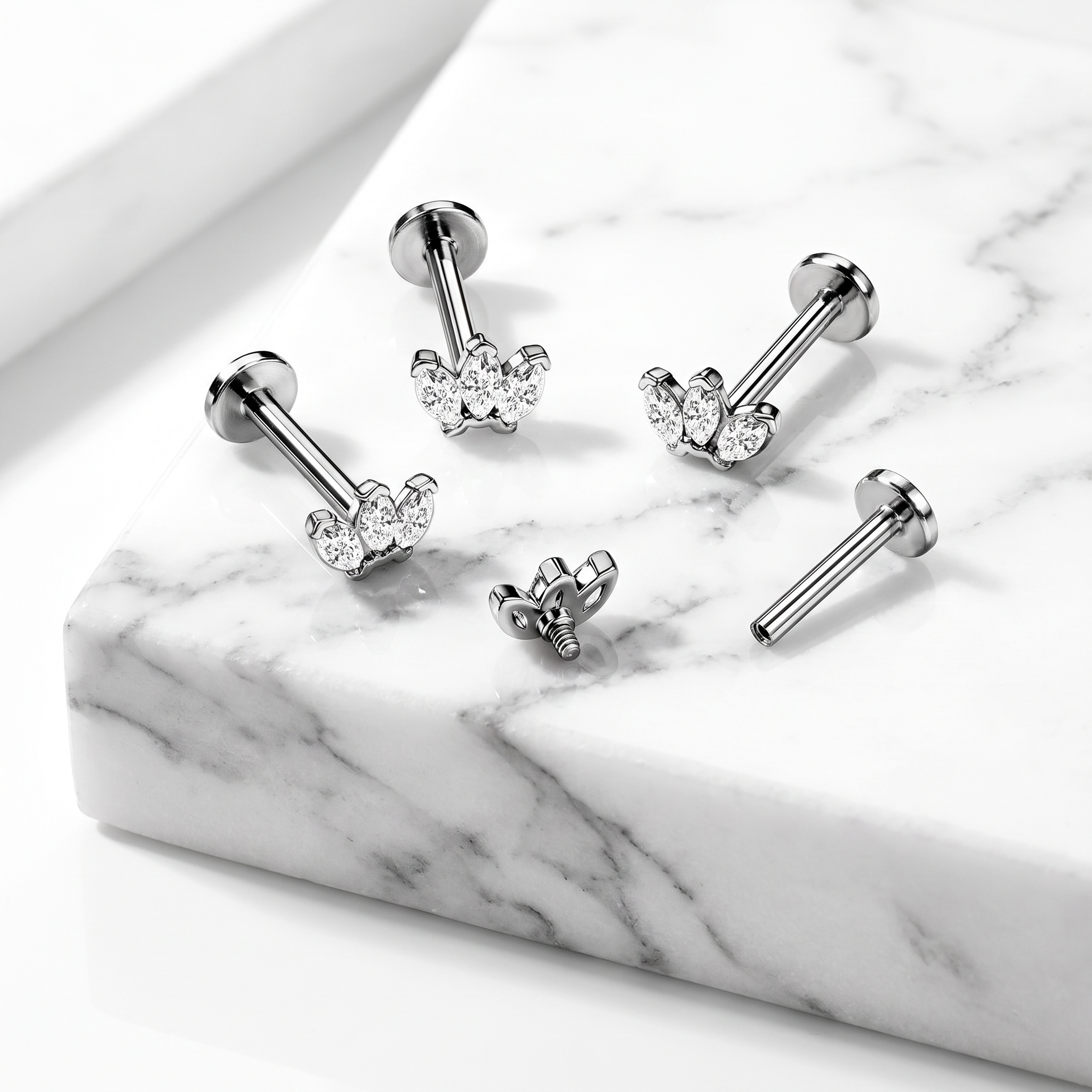 Four silver-toned barbell stud earrings with heart-shaped crystal clusters, arranged on a white marble slab.