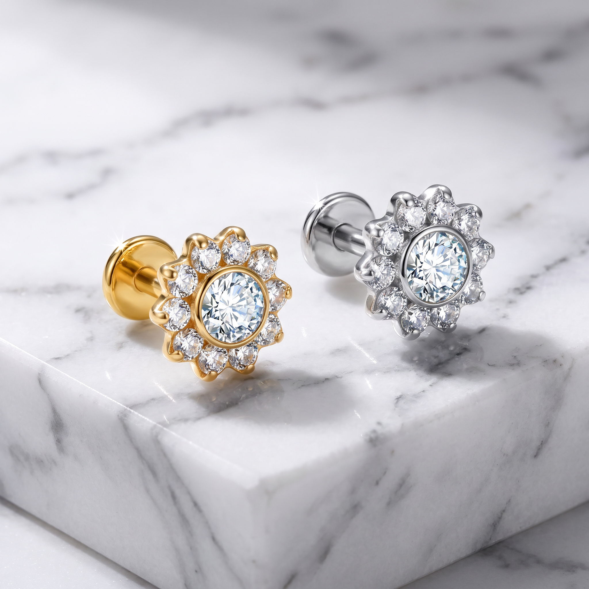 Two flower-shaped stud earrings with clear gemstones, one in yellow gold and one in silver, displayed on a white marble surface.