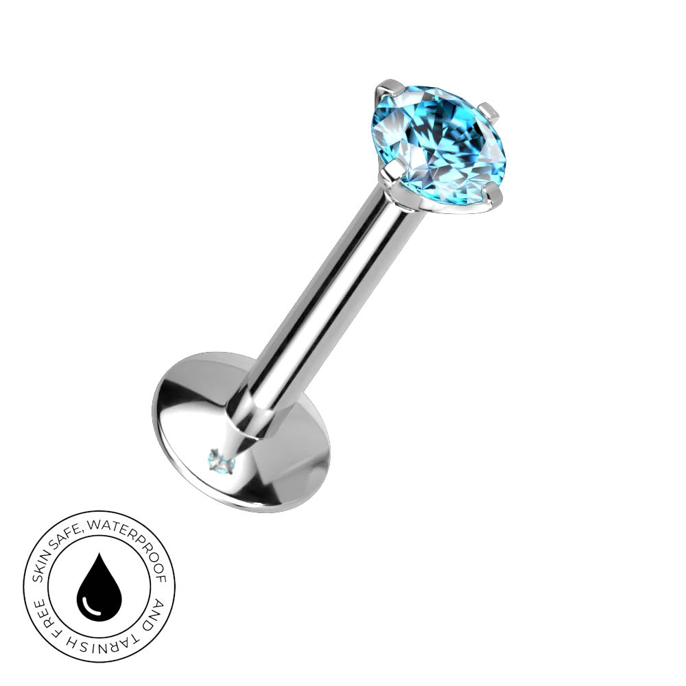 A silver-toned labret piercing barbell with a faceted light blue gemstone, shown on a plain white background with a circular 'Skin Safe Waterproof' badge in the lower-left corner.