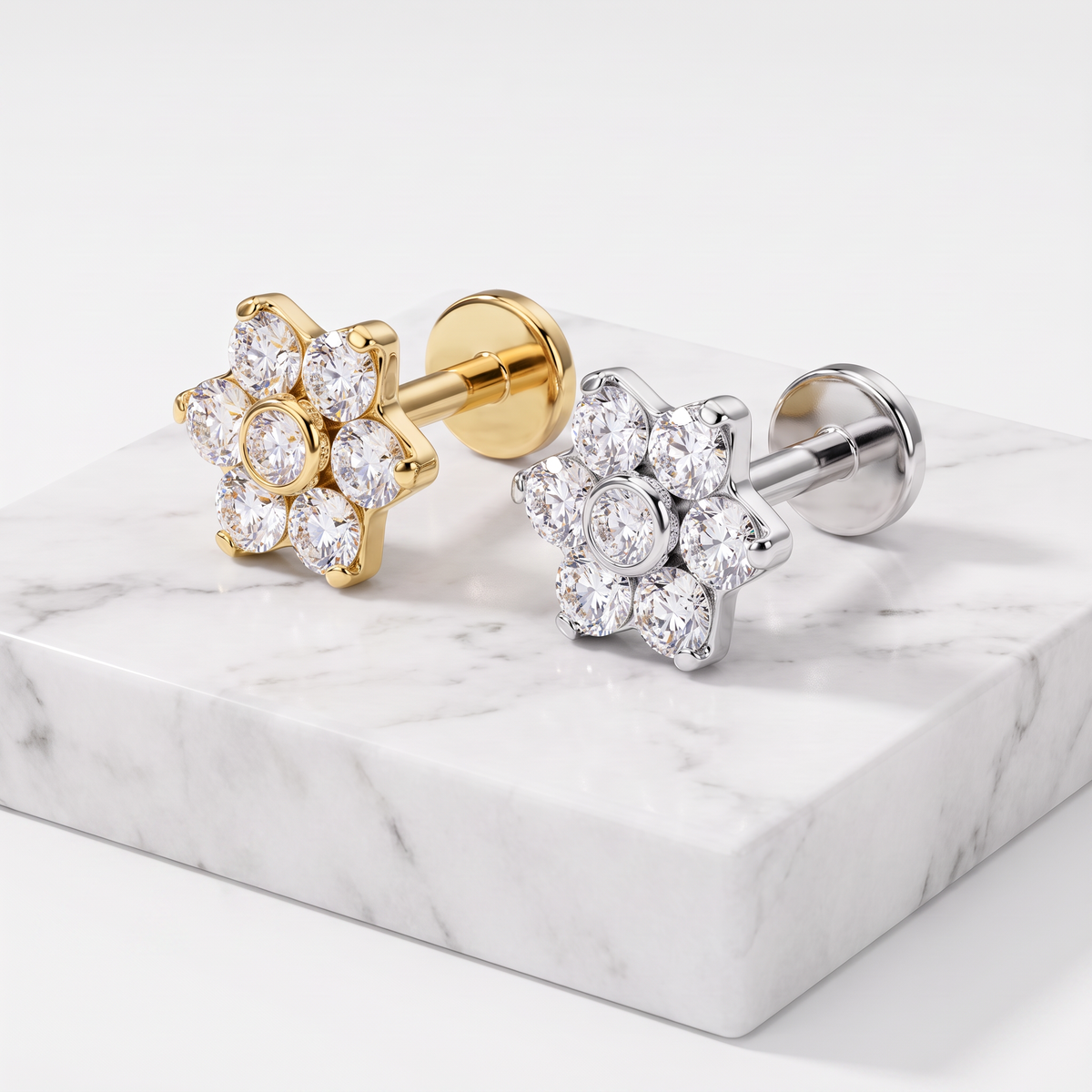 Two flower-shaped stud earrings displayed on a white marble block against a clean white background. One earring has a gold-tone metal setting with clear stones, and the other has a silver-tone metal setting with clear stones.