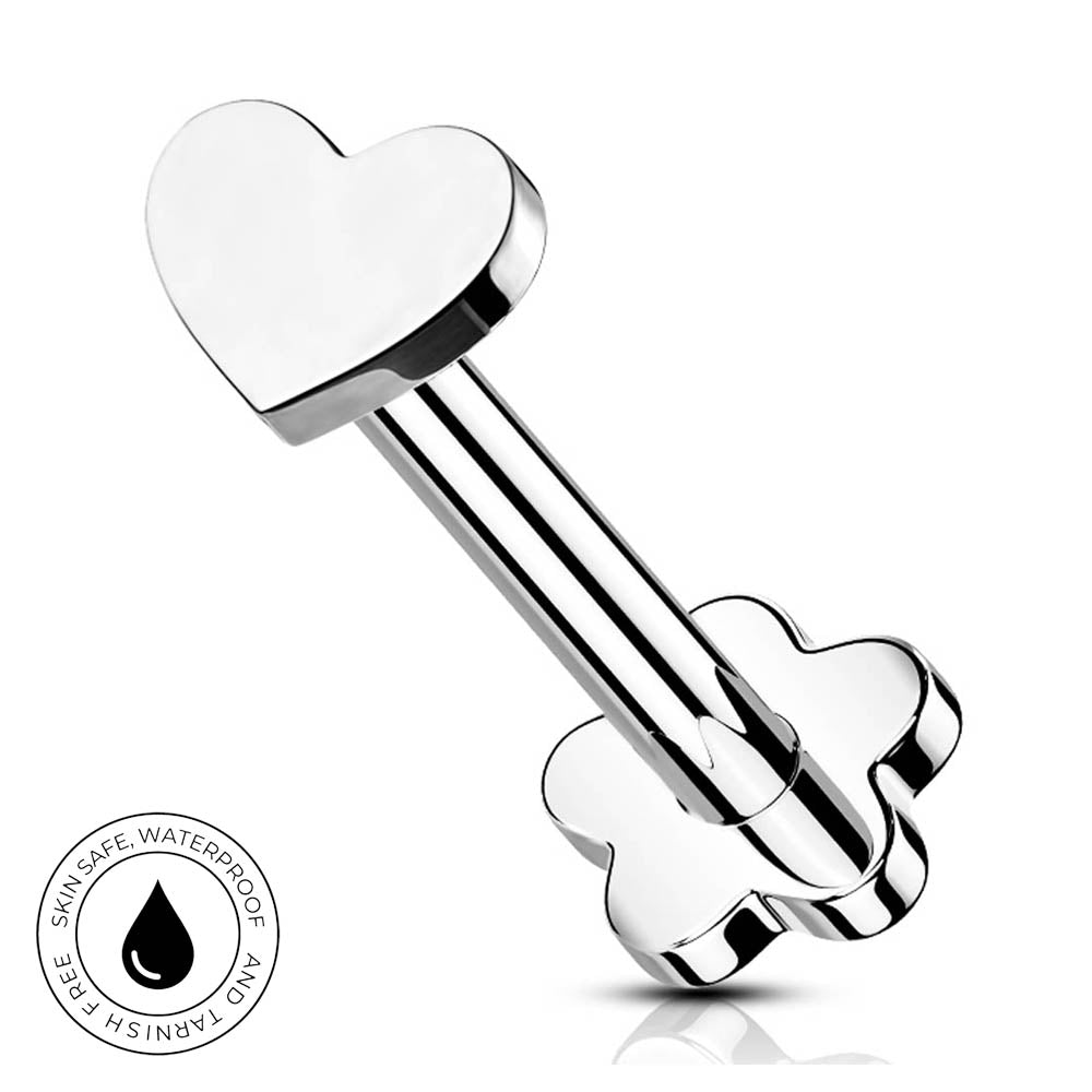A stainless steel barbell piercing stud with a polished heart-shaped end and a flower-shaped backing, shown on a white background with a small circular skin-safe waterproof badge in the lower-left corner.