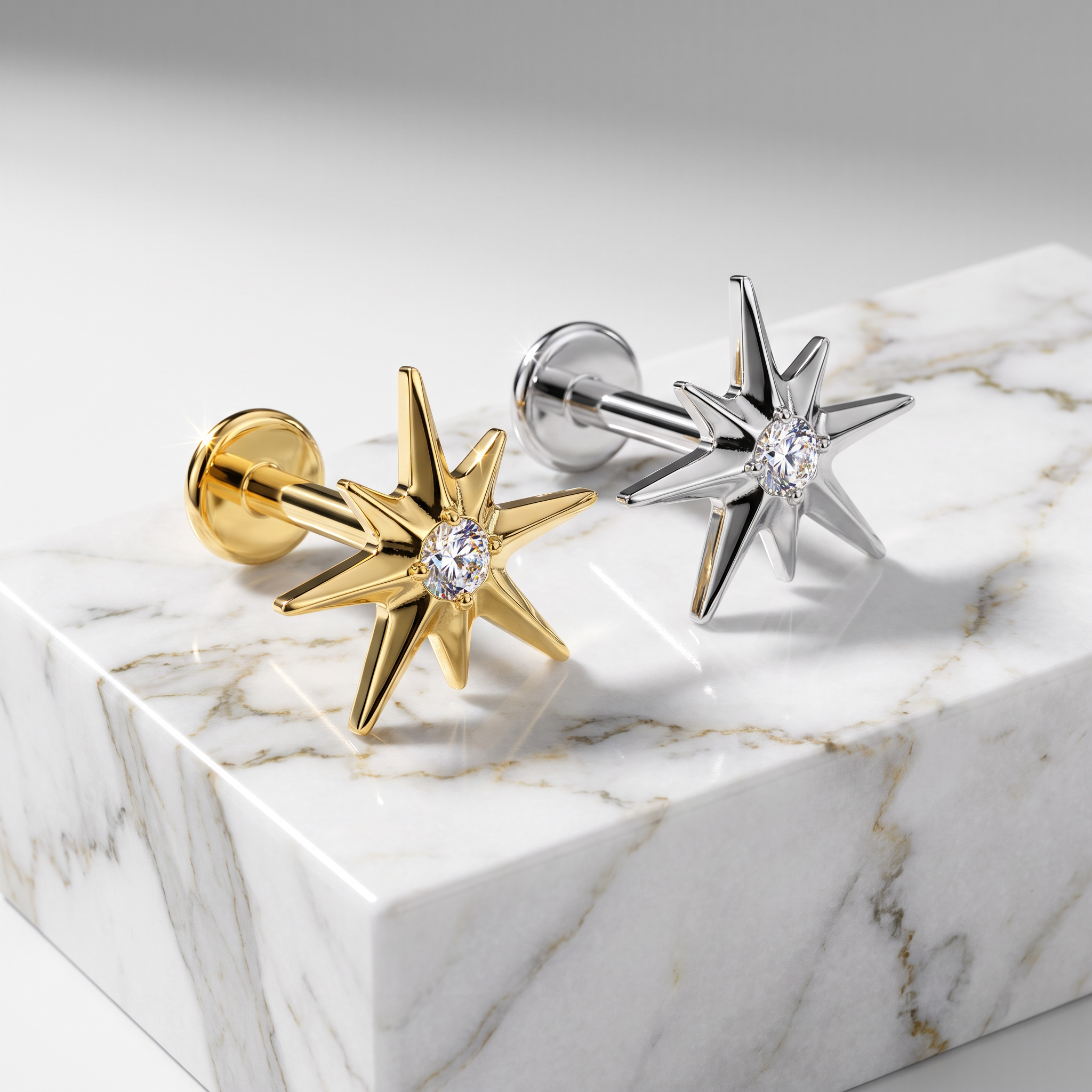 Two star-shaped stud earrings displayed on a white marble block. One earring is polished yellow gold with a clear central gemstone, and the other is polished silver with a matching clear gemstone.