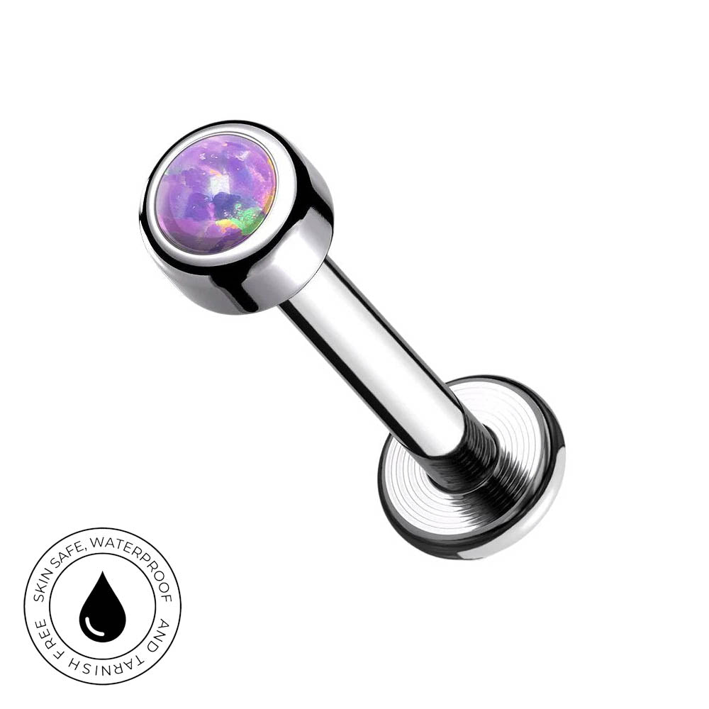A silver-toned flat-back labret piercing barbell with a round bezel-set iridescent purple and green gemstone. A circular 'Skin Safe Waterproof' badge is shown in the bottom-left corner against a plain white background.