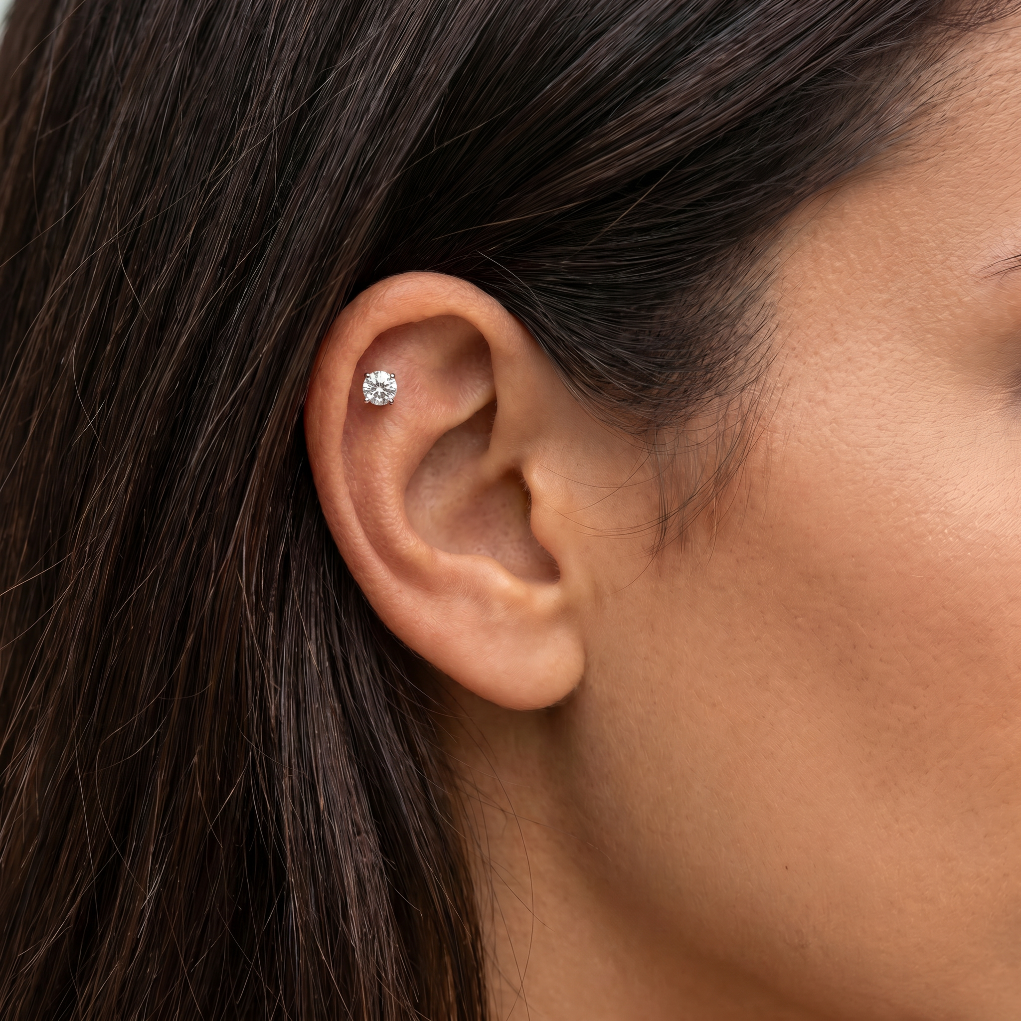 A close-up of a person's ear wearing a small round stud earring with a silver-toned metal setting and clear gemstone.