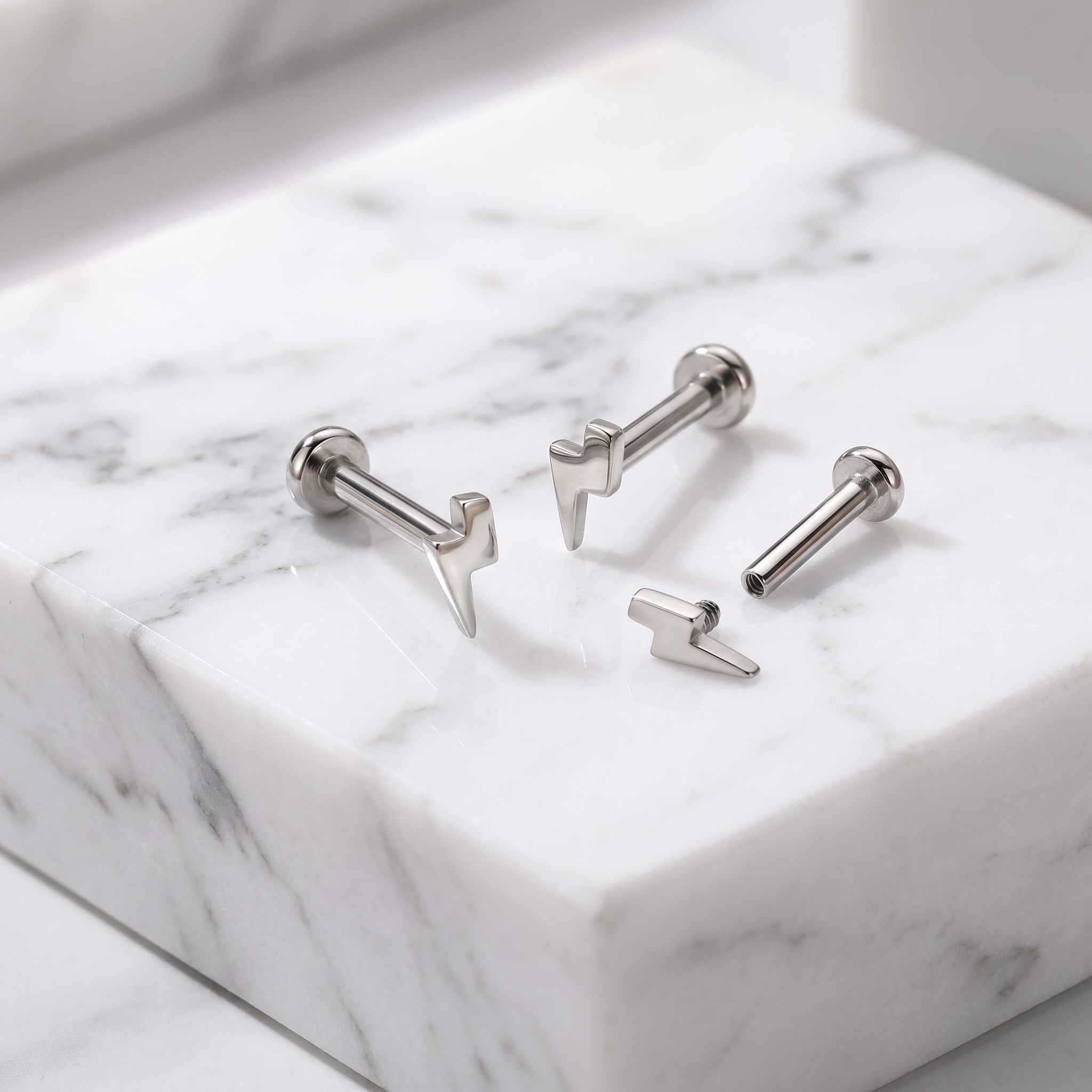 Four silver-toned lightning bolt stud earrings arranged on a white marble block with gray veining.