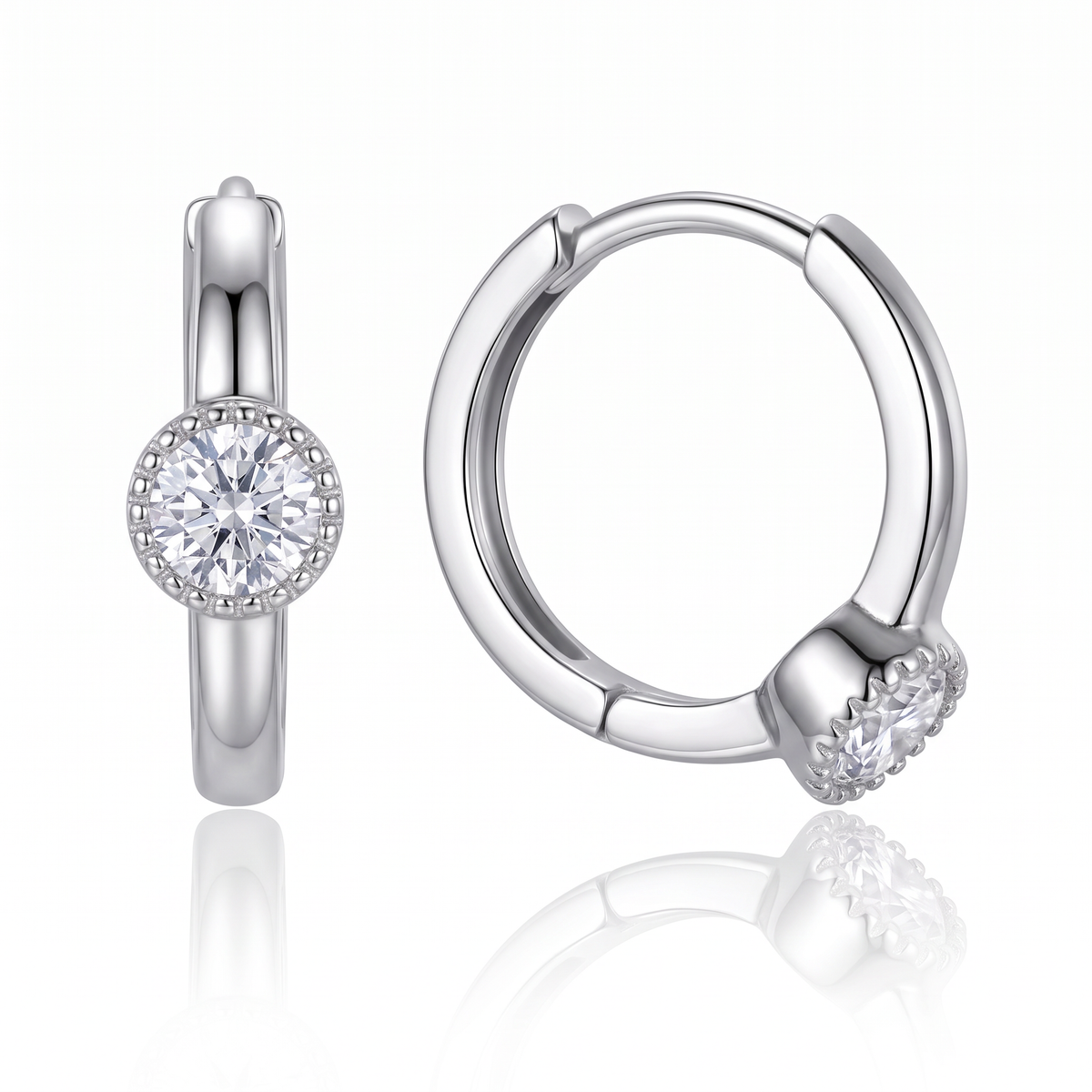 A pair of polished silver huggie hoop earrings, one shown from the front with a round clear gemstone in a halo setting and the other from the side showing the hinge and the gemstone setting, on a white background with a soft reflection.