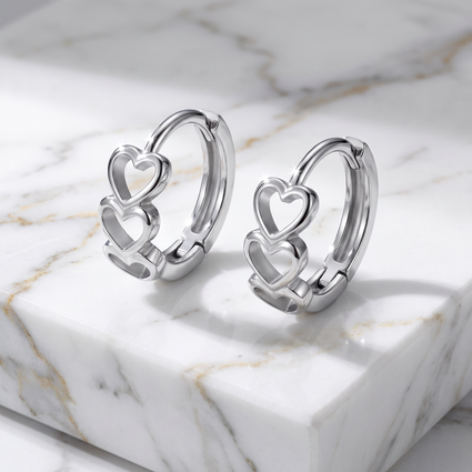 A pair of polished silver huggie hoop earrings with interlocking open heart designs, displayed on a white marble block with gold veining.