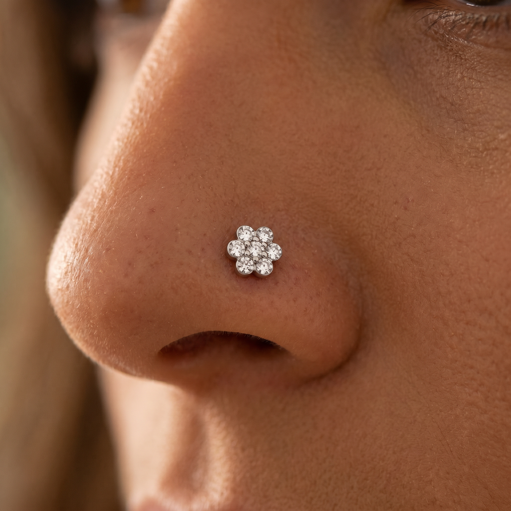 A close-up of a person's nose wearing a small flower-shaped stud earring made of clear gemstones in a silver-toned setting.