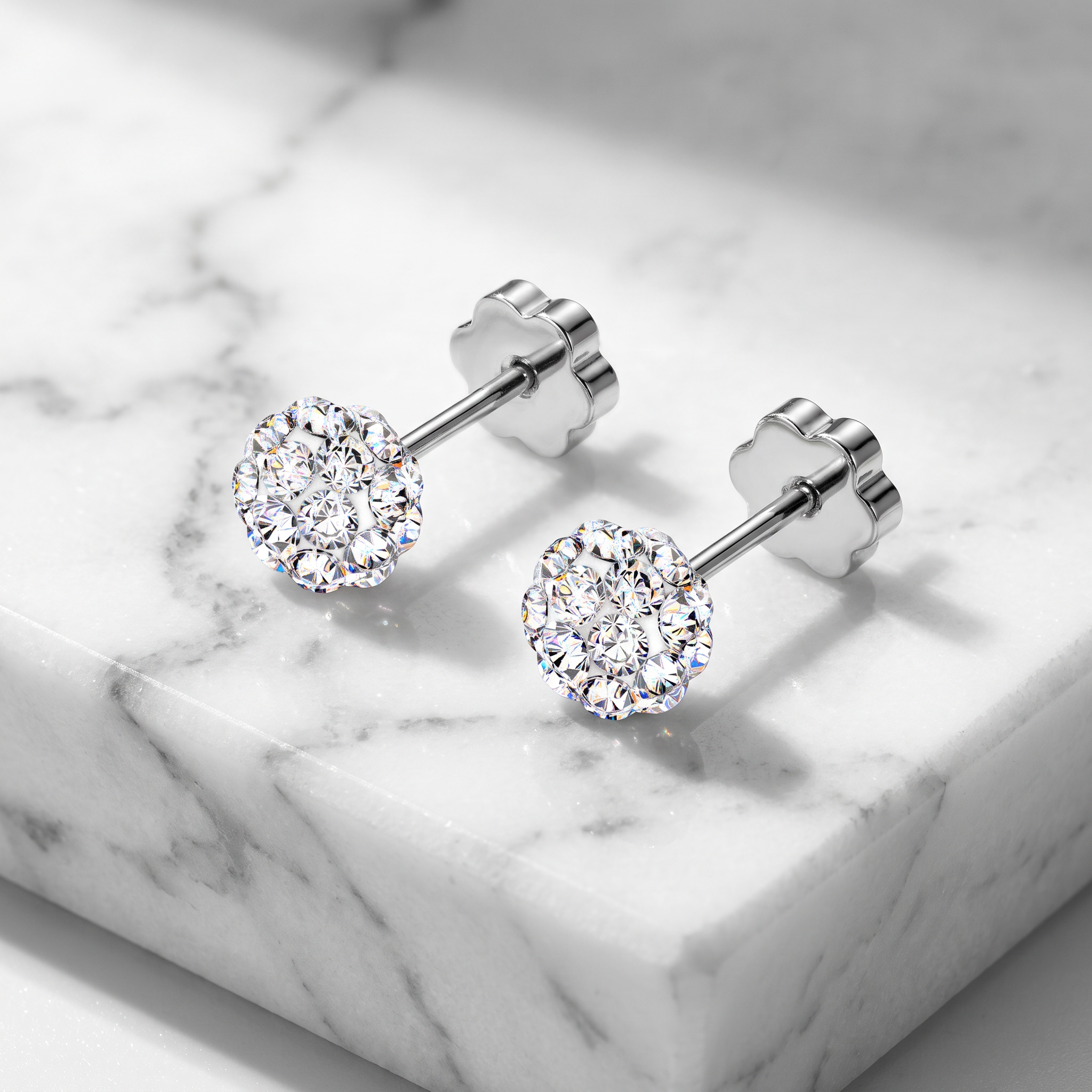 A pair of round-cut diamond stud earrings in a silver-toned setting, displayed on a white marble block.