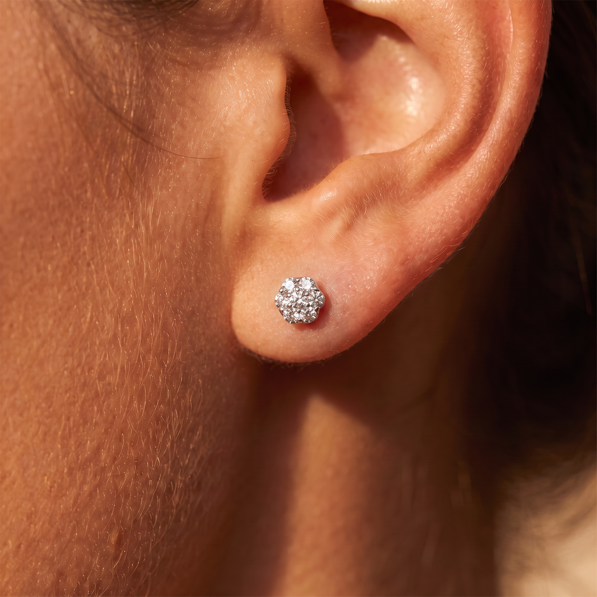 A close-up of a person's ear wearing a small round cluster stud earring with sparkling clear stones in a silver-toned setting.