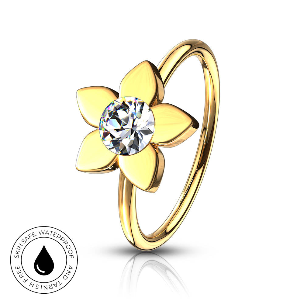 A gold flower-shaped ring with a clear round-cut gemstone in the center, shown on a white background with a reflection below and a small circular 'skin-safe waterproof' badge in the lower left.