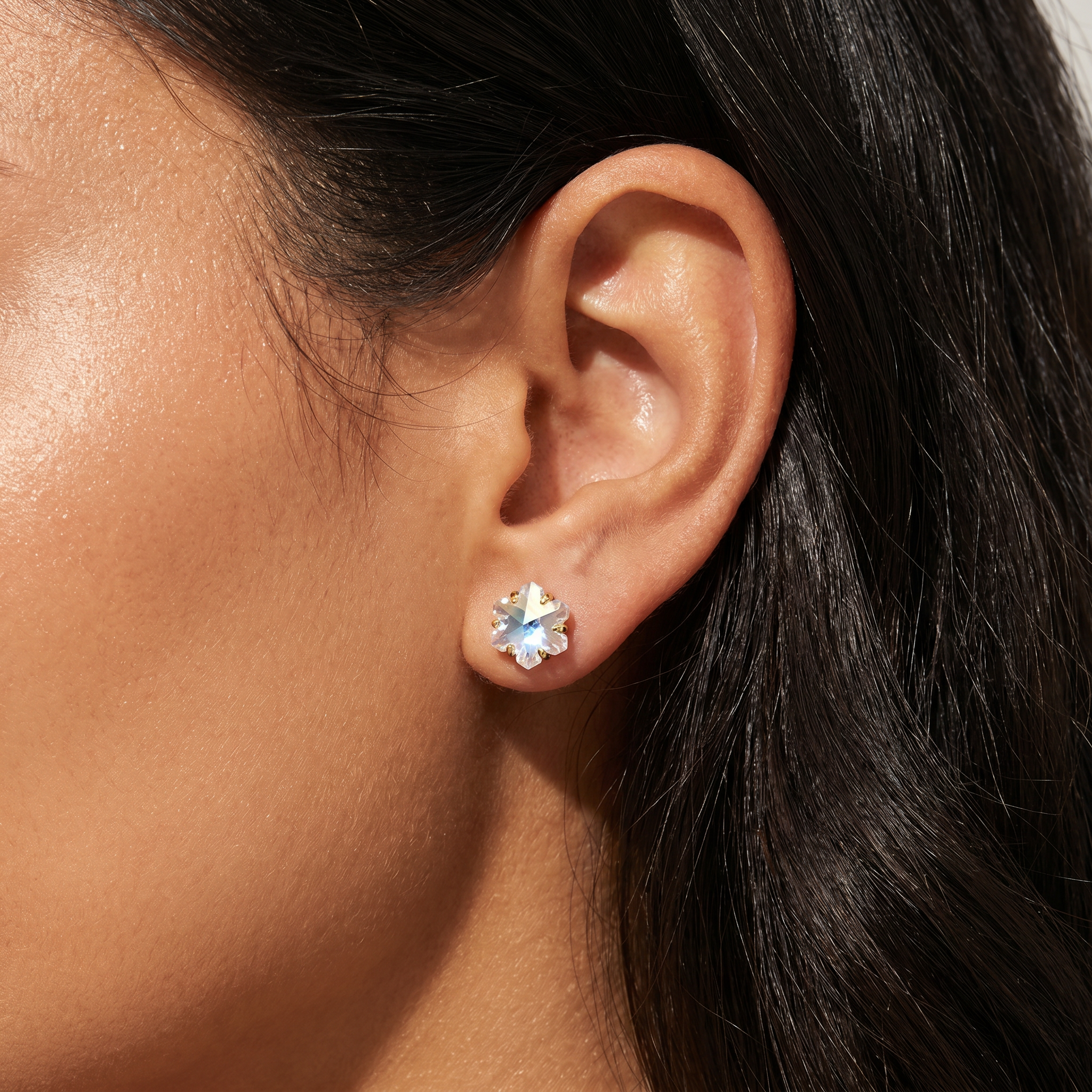 A close-up of a person's ear wearing a small silver-toned stud earring with a clear faceted flower-shaped crystal.