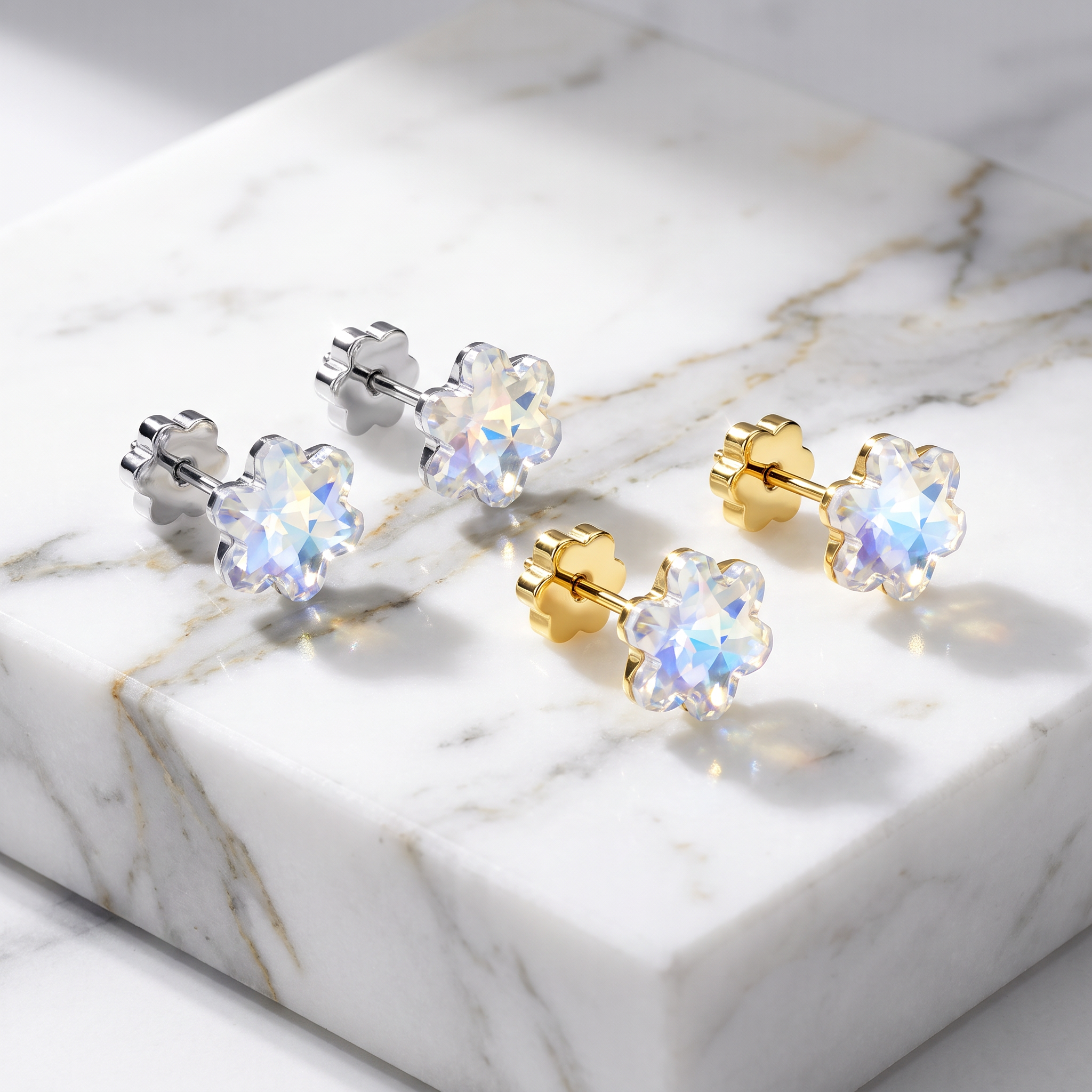 Four flower-shaped stud earrings with iridescent clear gemstones and gold or silver posts, arranged on a white marble slab.