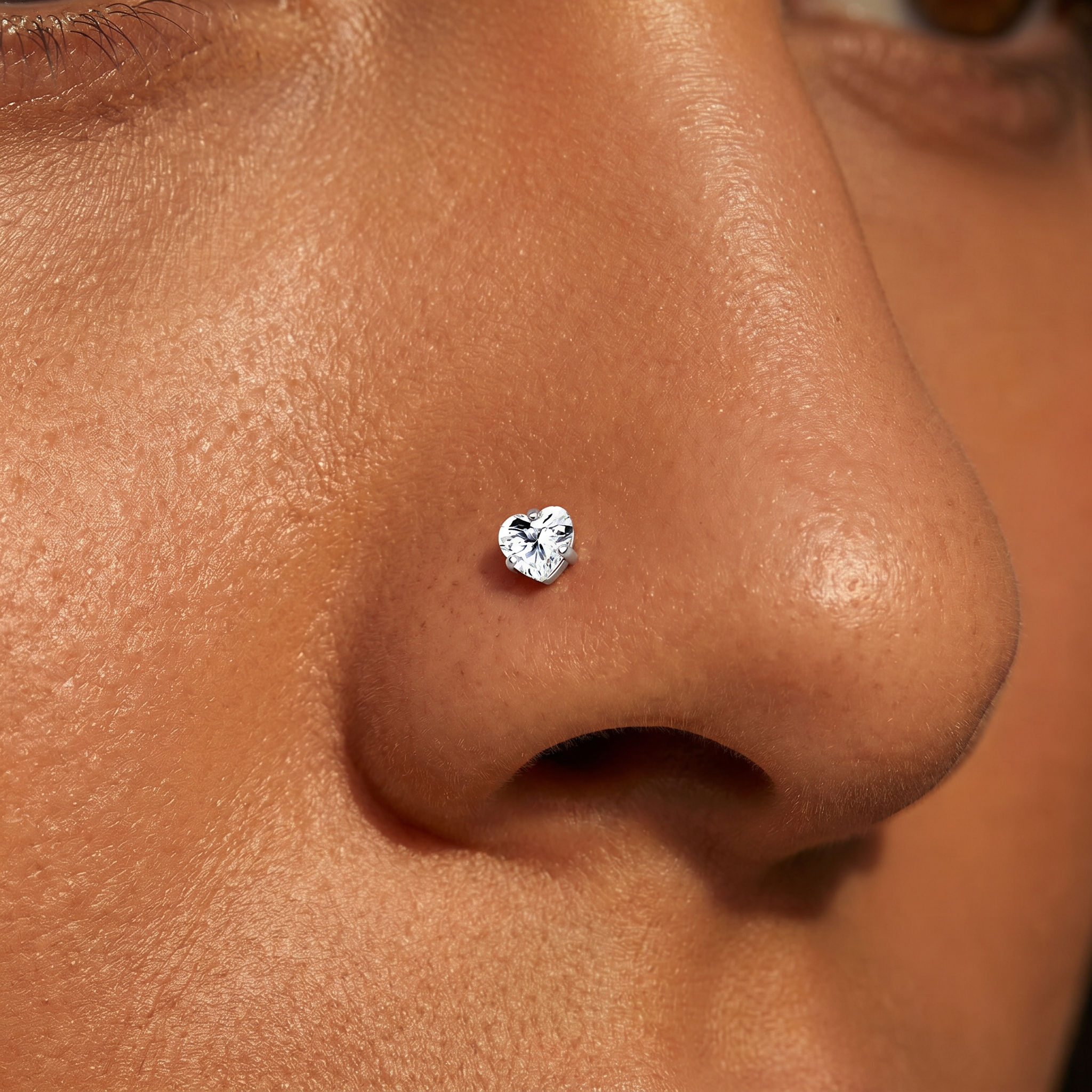 A close-up of a person's nose wearing a small heart-shaped silver stud earring.