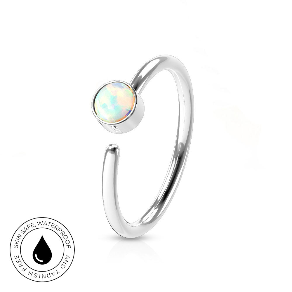 A silver-toned open ring with a round iridescent opal-like stone, shown on a clean white background. A small circular badge in the lower left reads 'SKINSAFE WATERPROOF AND TARNISH FREE' with a black droplet icon.