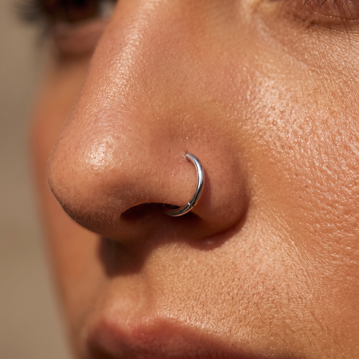 A close-up of a person's nose wearing a thin silver crescent hoop nose ring.