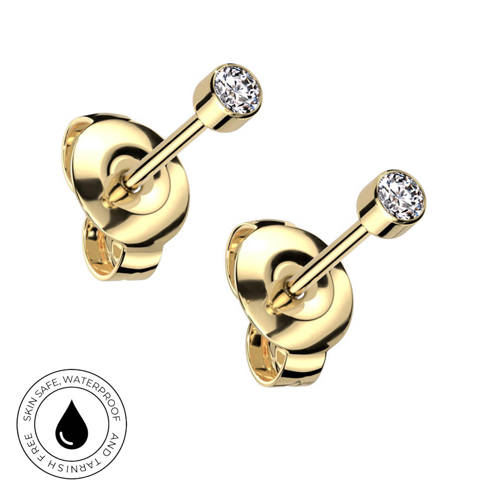A pair of gold cartilage piercings with round clear gemstones, shown from the back on a white background with a circular skin-safe waterproof badge in the bottom-left corner.