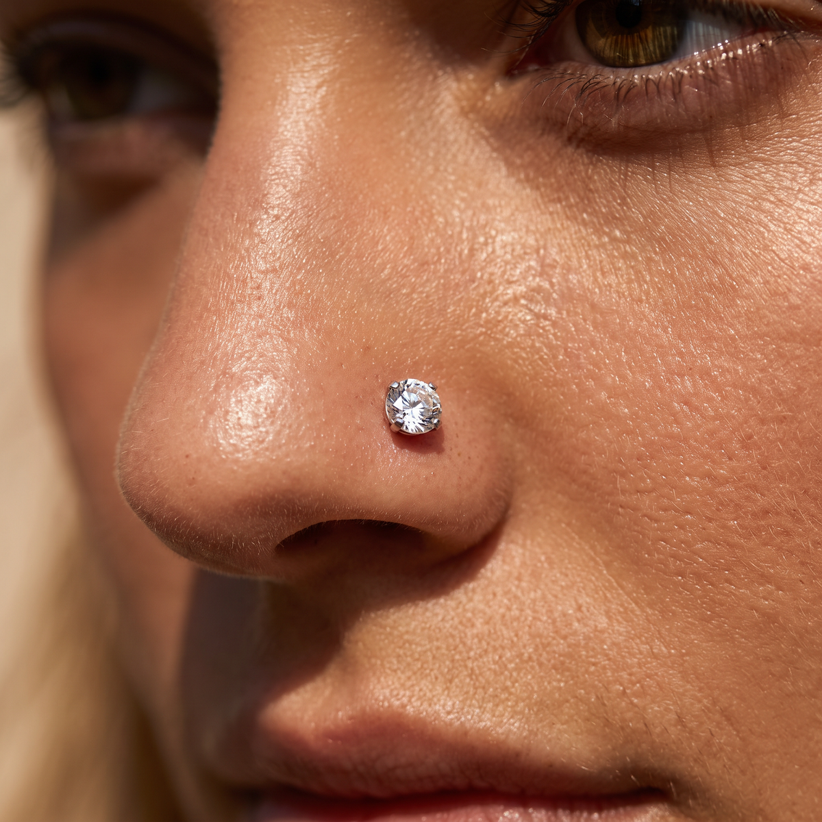 A close-up of a person's nose wearing a single round brilliant-cut clear gemstone stud earring.
