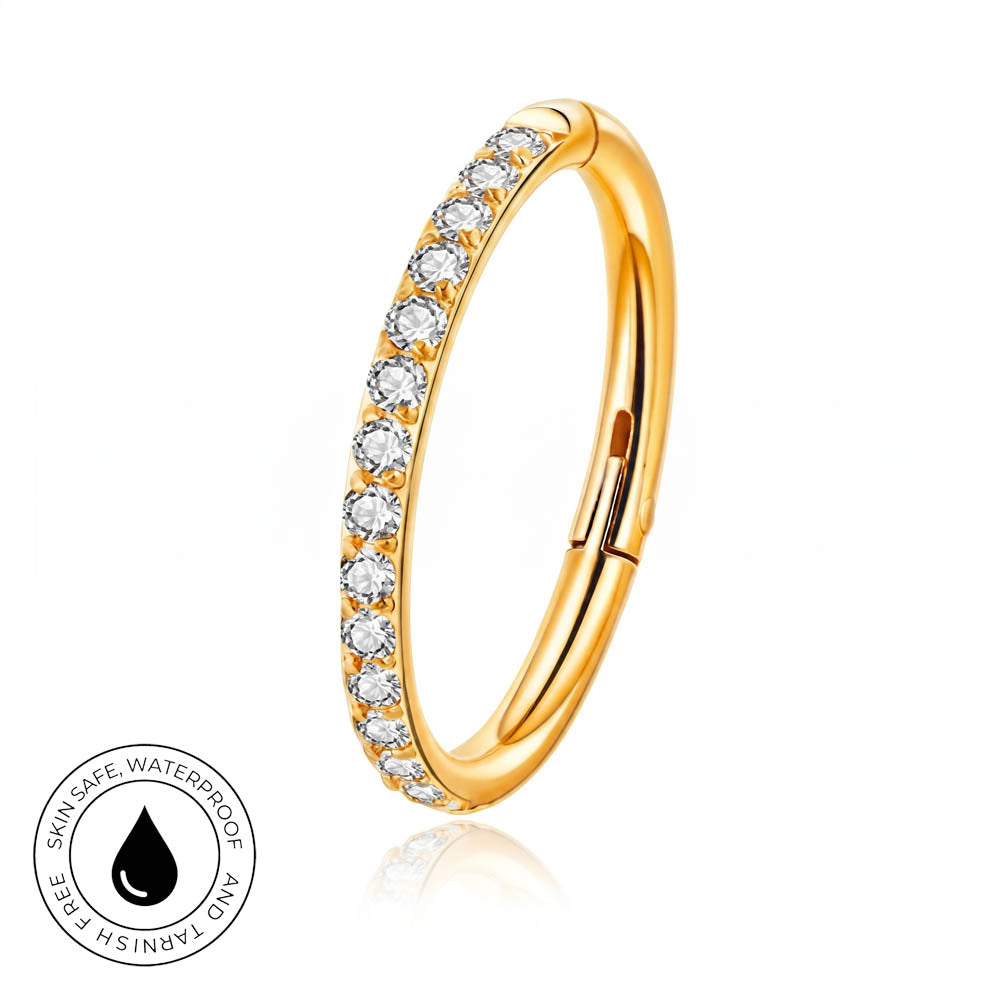 A gold-plated curved ring with a row of clear gemstones on one side, shown on a white background with a small circular 'skin-safe waterproof' badge in the lower left.