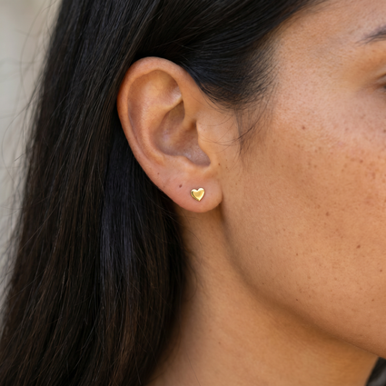 A close-up of a person's ear wearing a small gold heart stud earring.