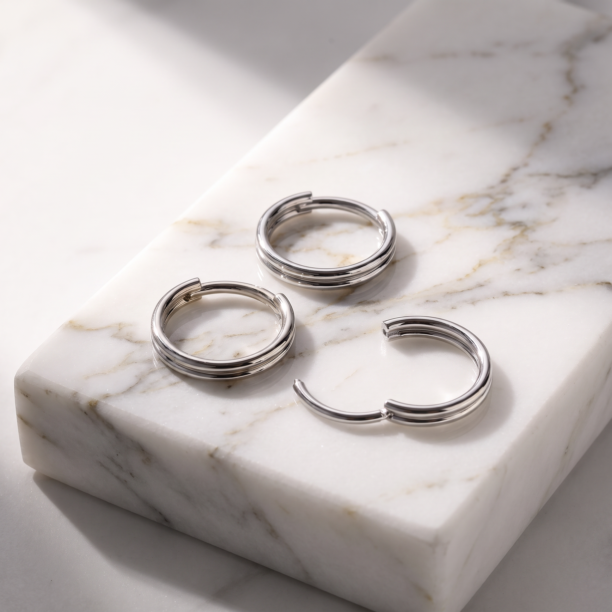 Three silver hoop earrings with a triple-band design, displayed on a white marble block with gray veining.